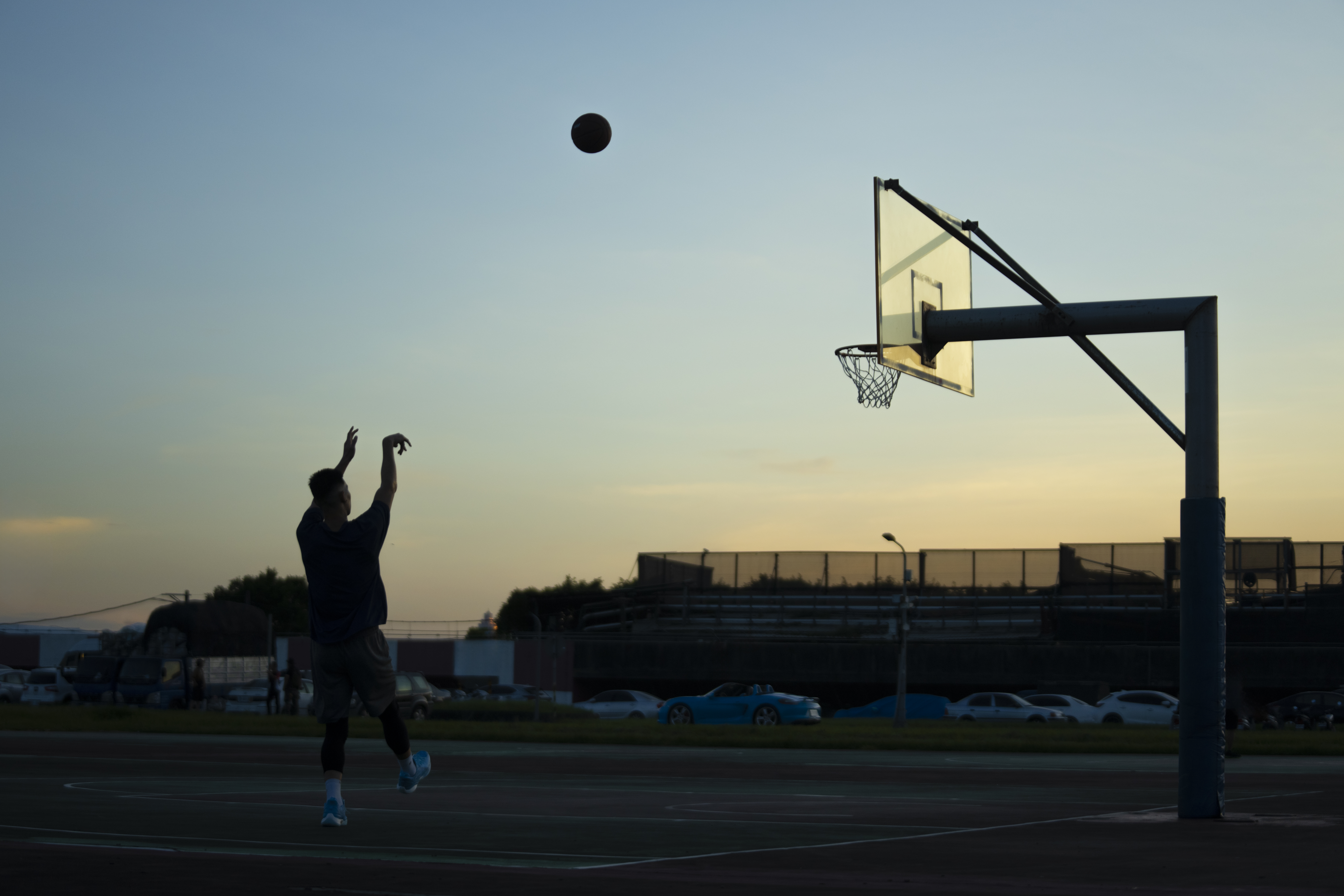 Jeremy Lin in silhouette shoots basketball towards net at dusk