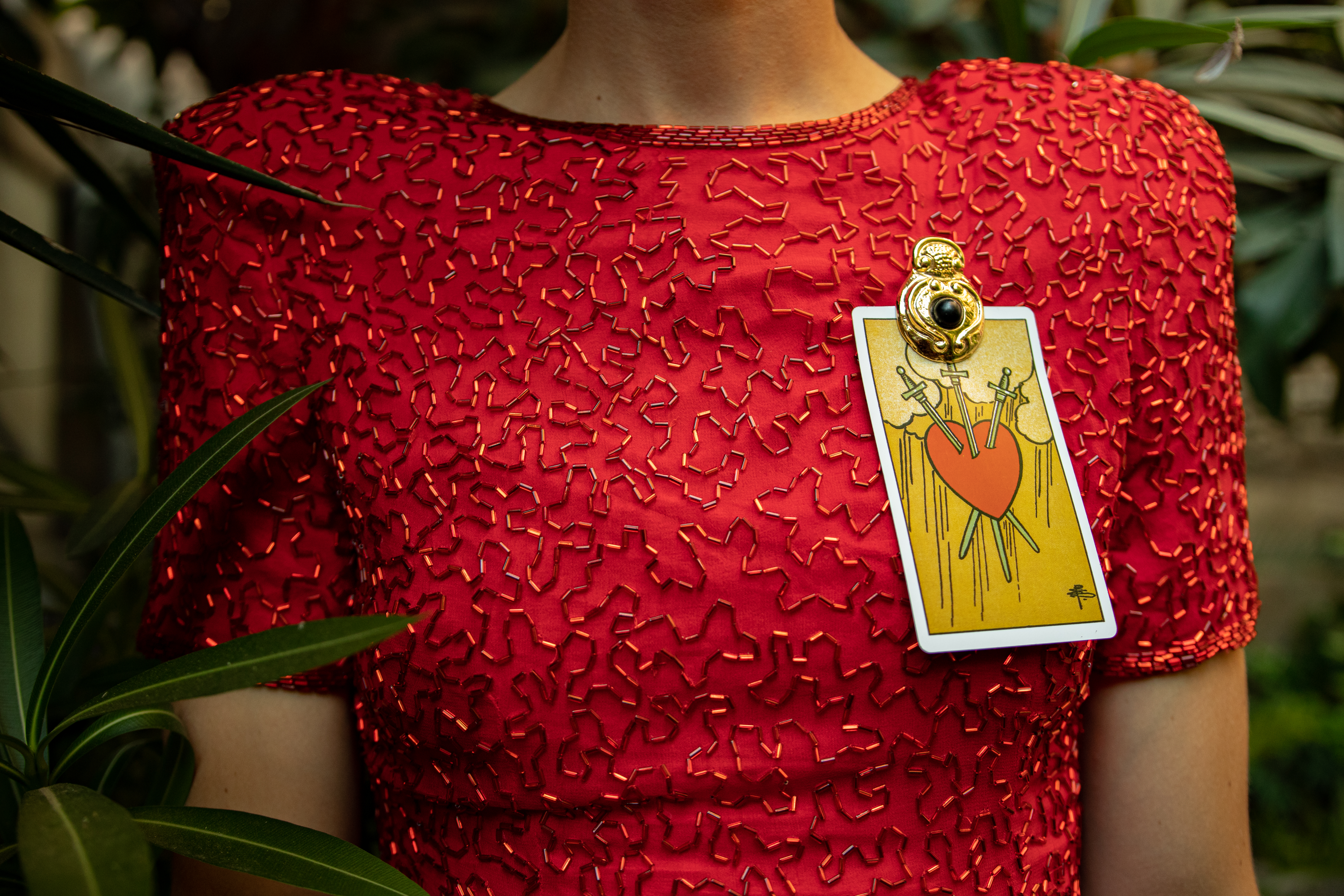 A closeup of a red formal dress with a playing card pinned to it.