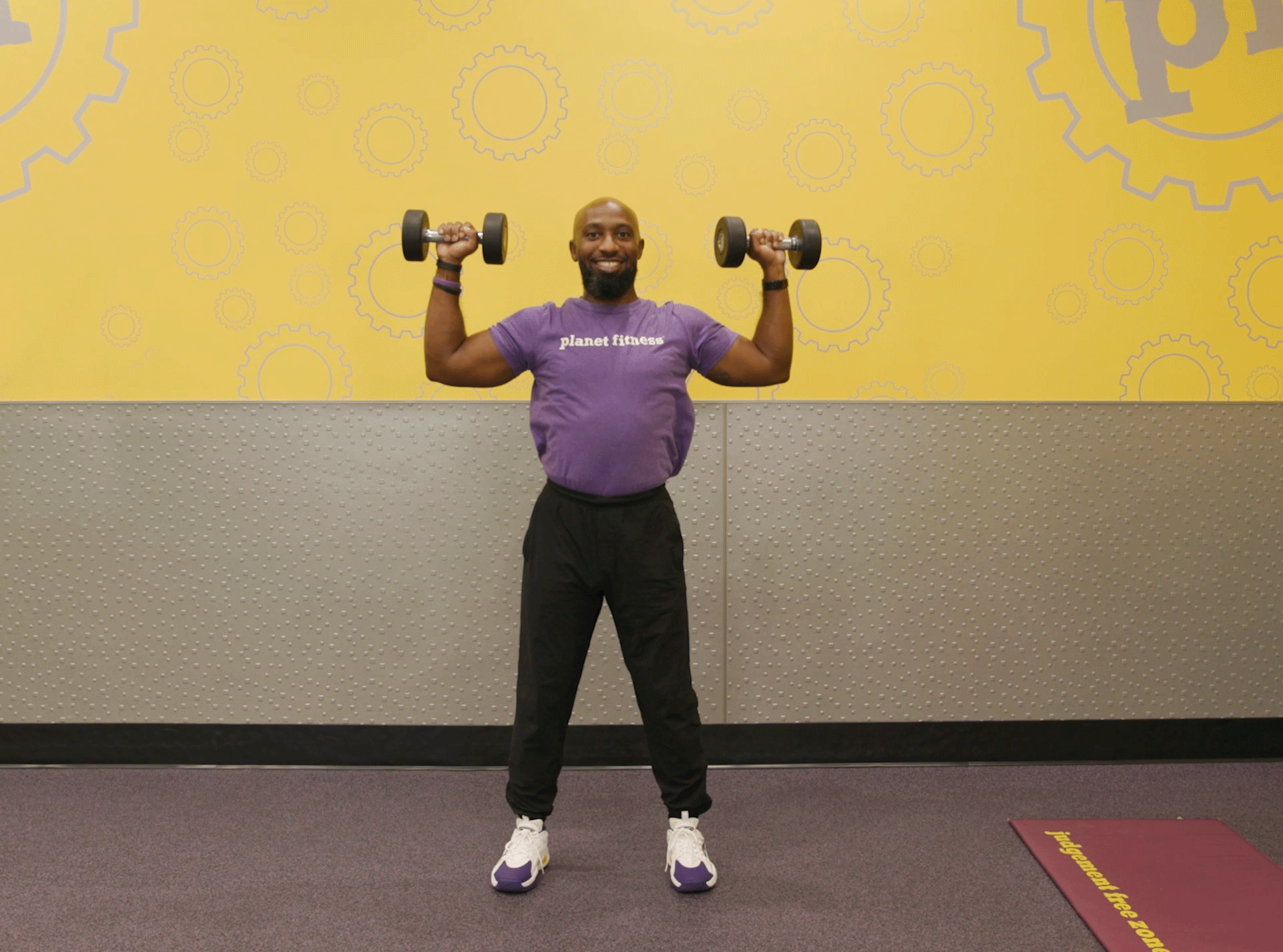 Man performing shoulder press exercise with dumbbells in Planet Fitness club