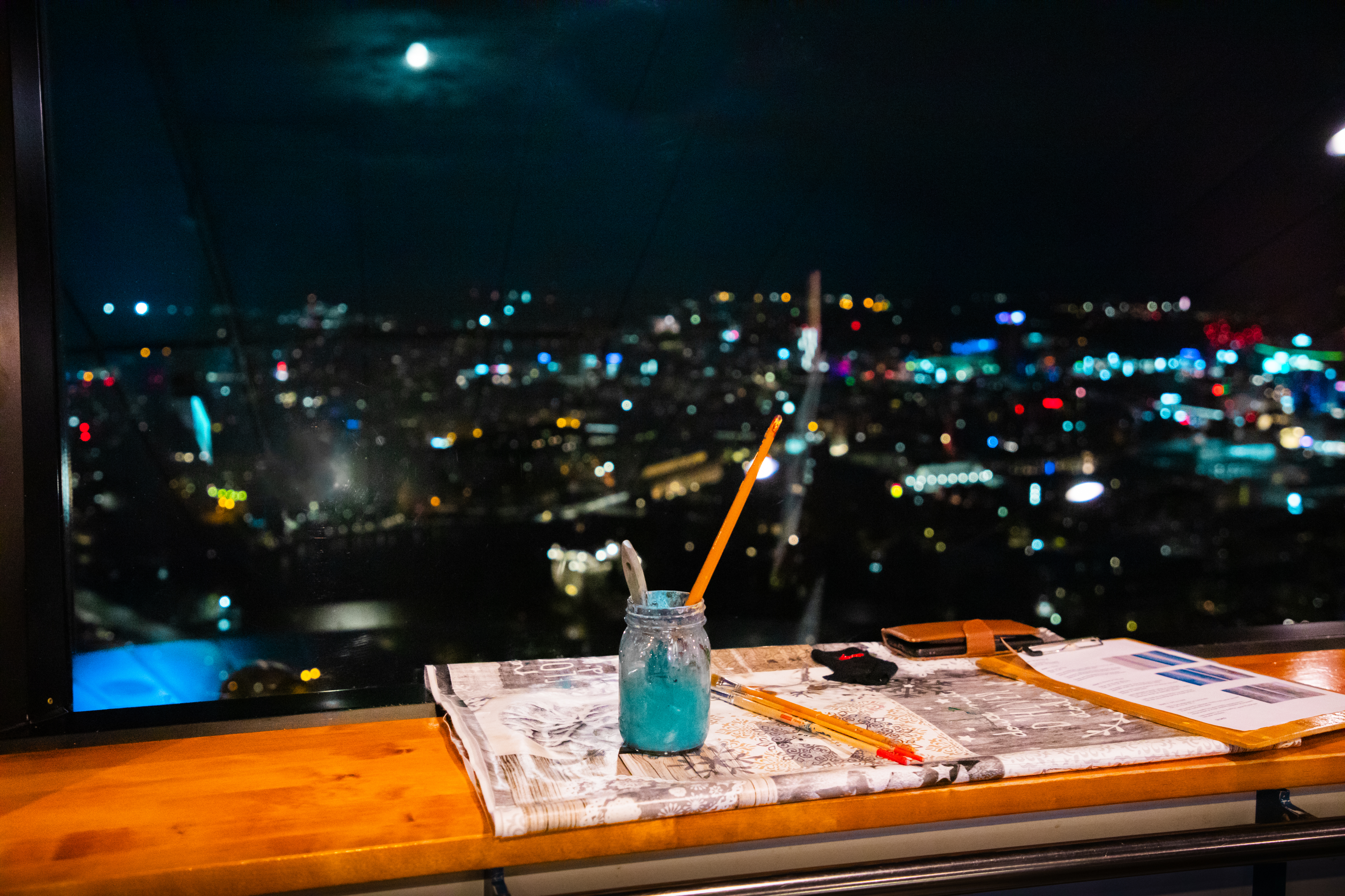 Vesipurkki Neula Sky Cafen ikkunalaudalla pimeän, valaistun kaupungin edustalla kuun loisteessa.