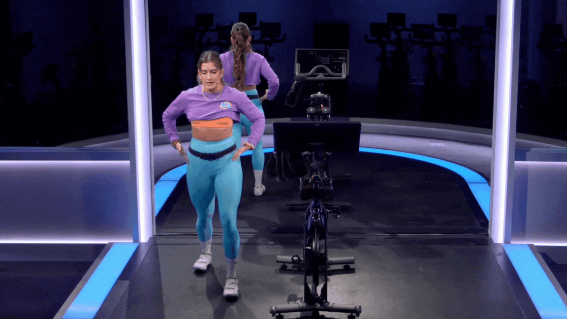 Peloton instructor Camila Ramón demonstrates a standing calf and hip flexor stretch during a Peloton post-ride stretch class.