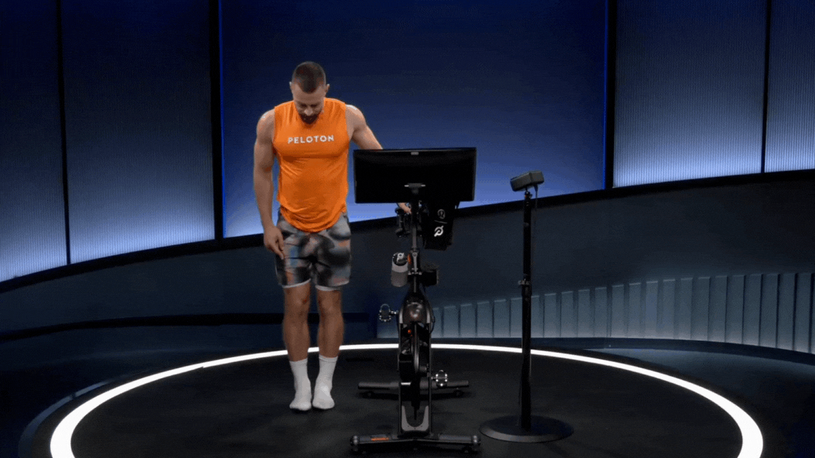 Peloton instructor Erik Jäger demonstrates a cross-legged standing side stretch during a Peloton stretch class.