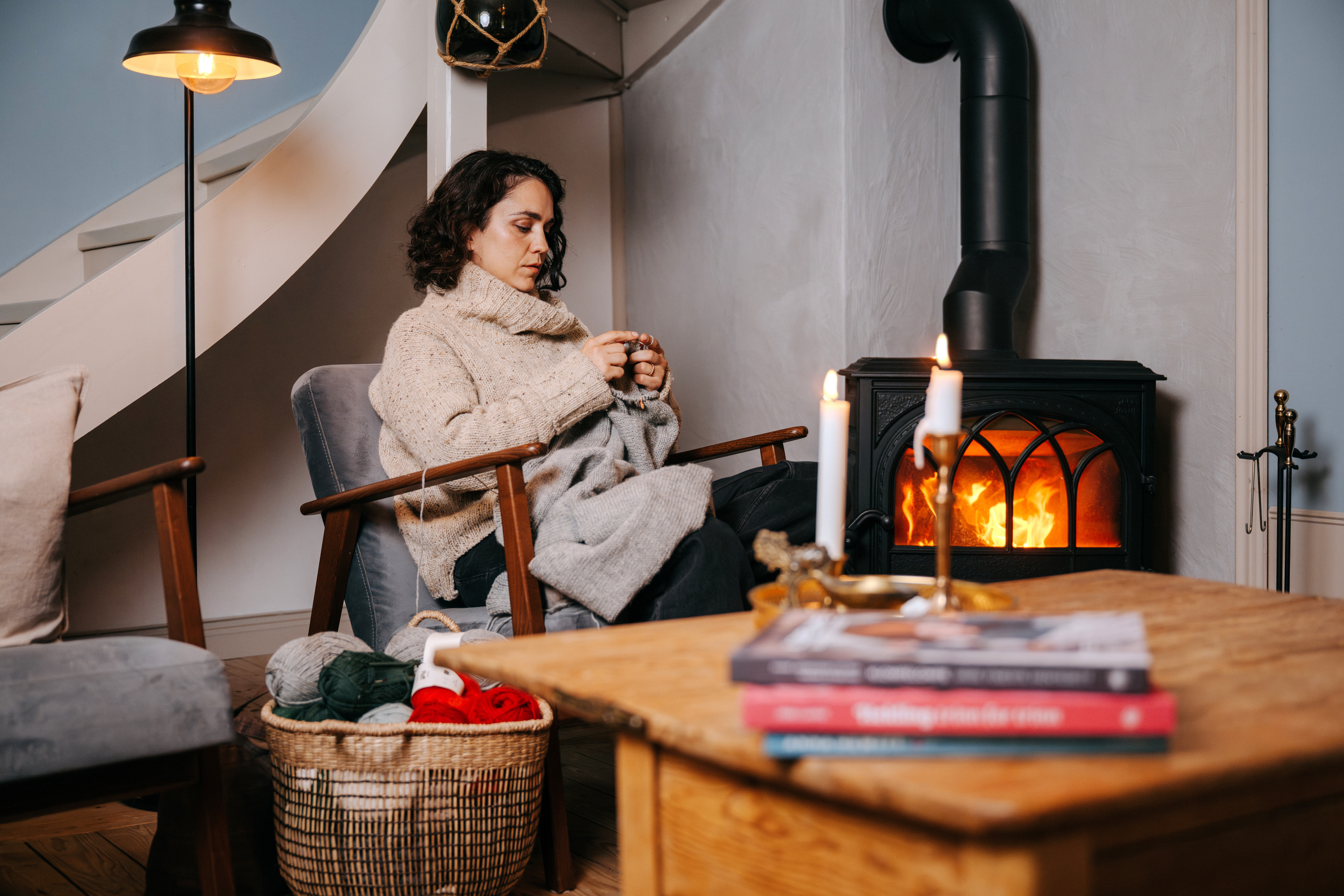 Person som stickar ett grått plagg i en varm och hemtrevlig miljö.