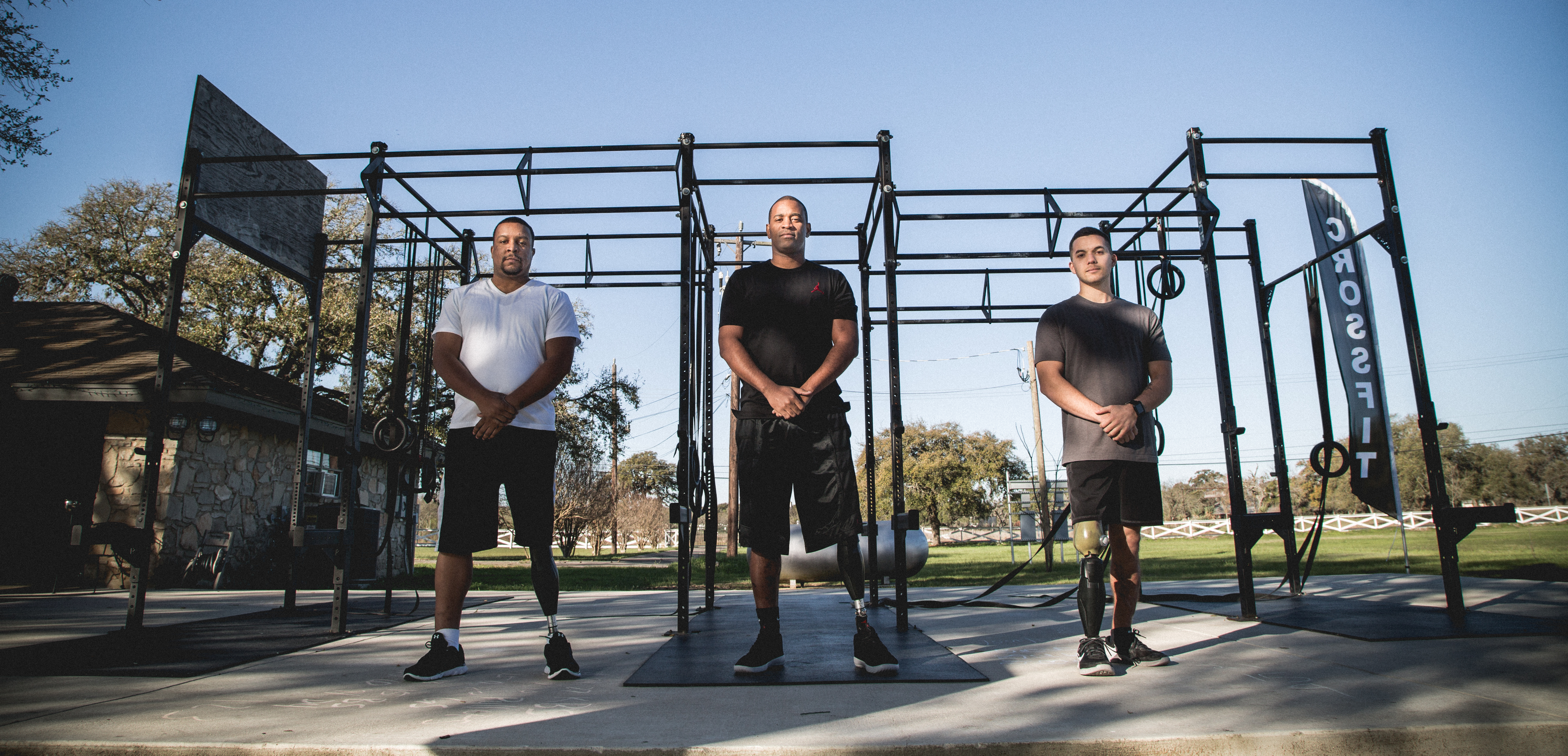 Three male amputee veterans stand side by side in a workout area and pose for the camera