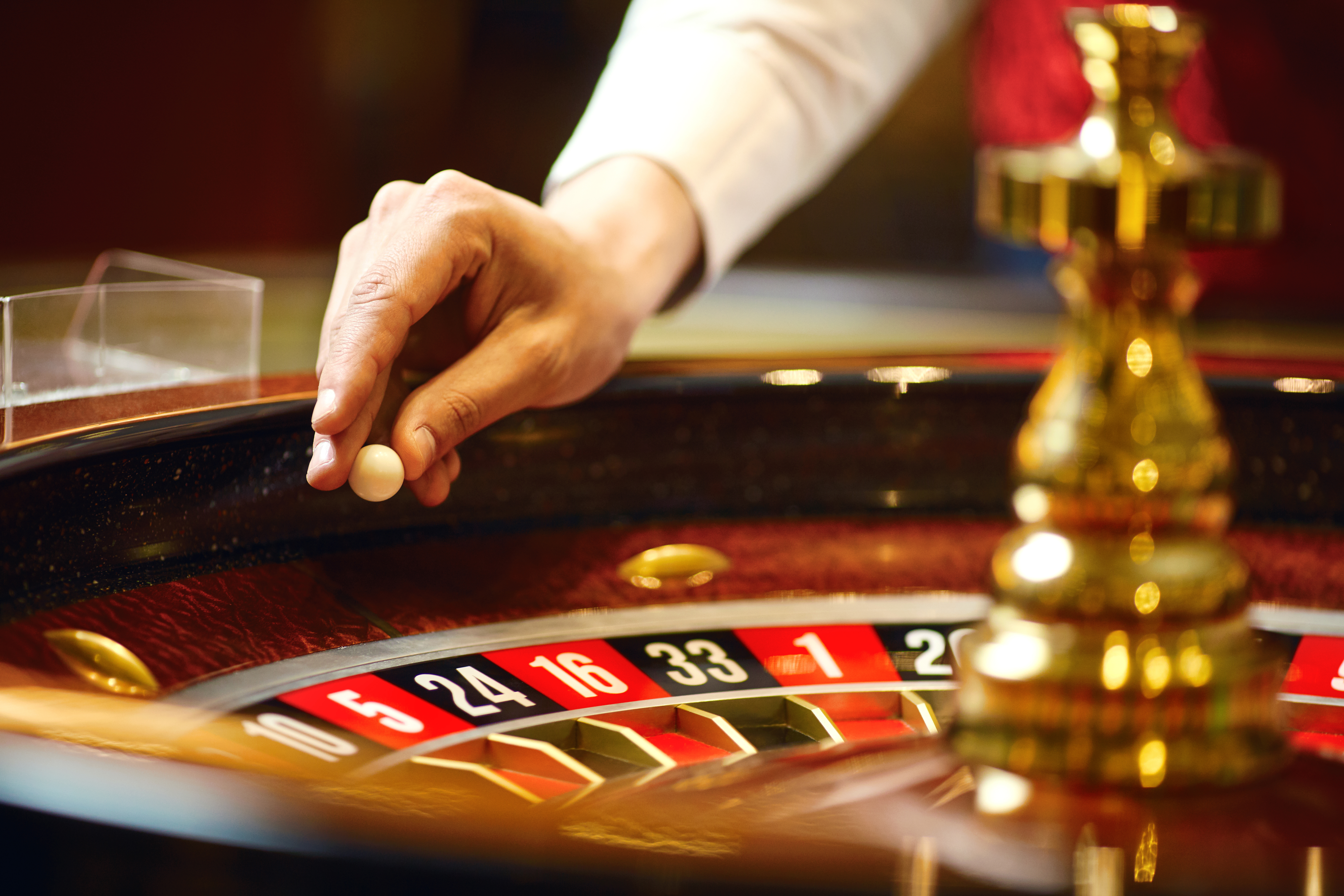 Croupier holding a roulette ball above a roulette wheel.