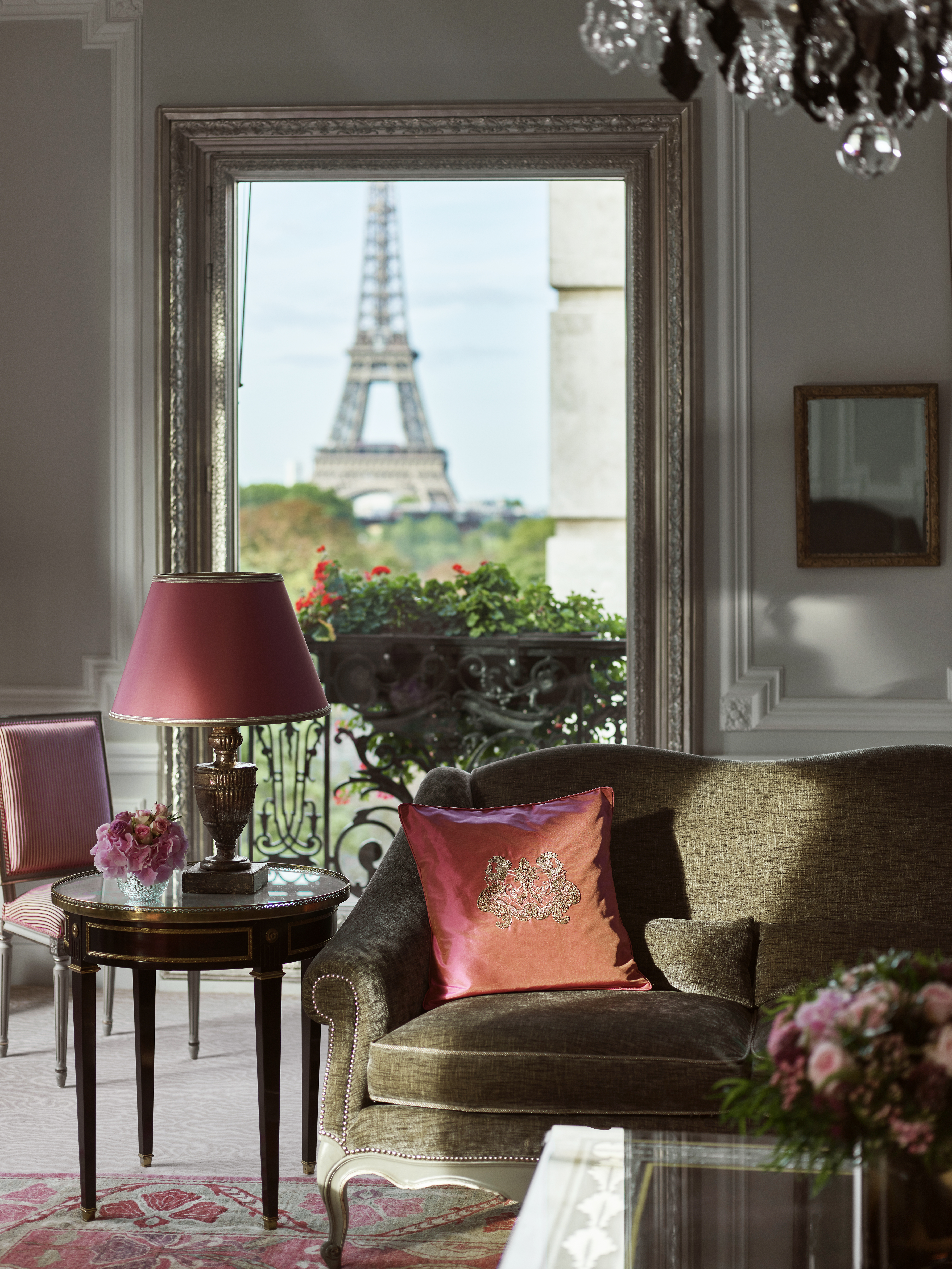 View of Eiffel Tower from the elegant living room of The Plaza Athenee, with a red table lamp, dark green sofa and red cushion