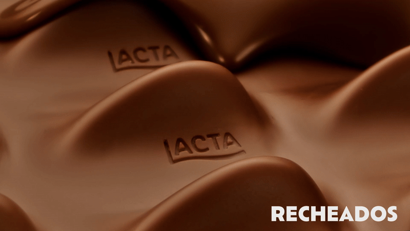 Close-up de tabletes de chocolate Lacta Recheados quebrados, revelando recheio cremoso com pedaços de biscoito sendo cobertos por uma onda de chocolate derretido.