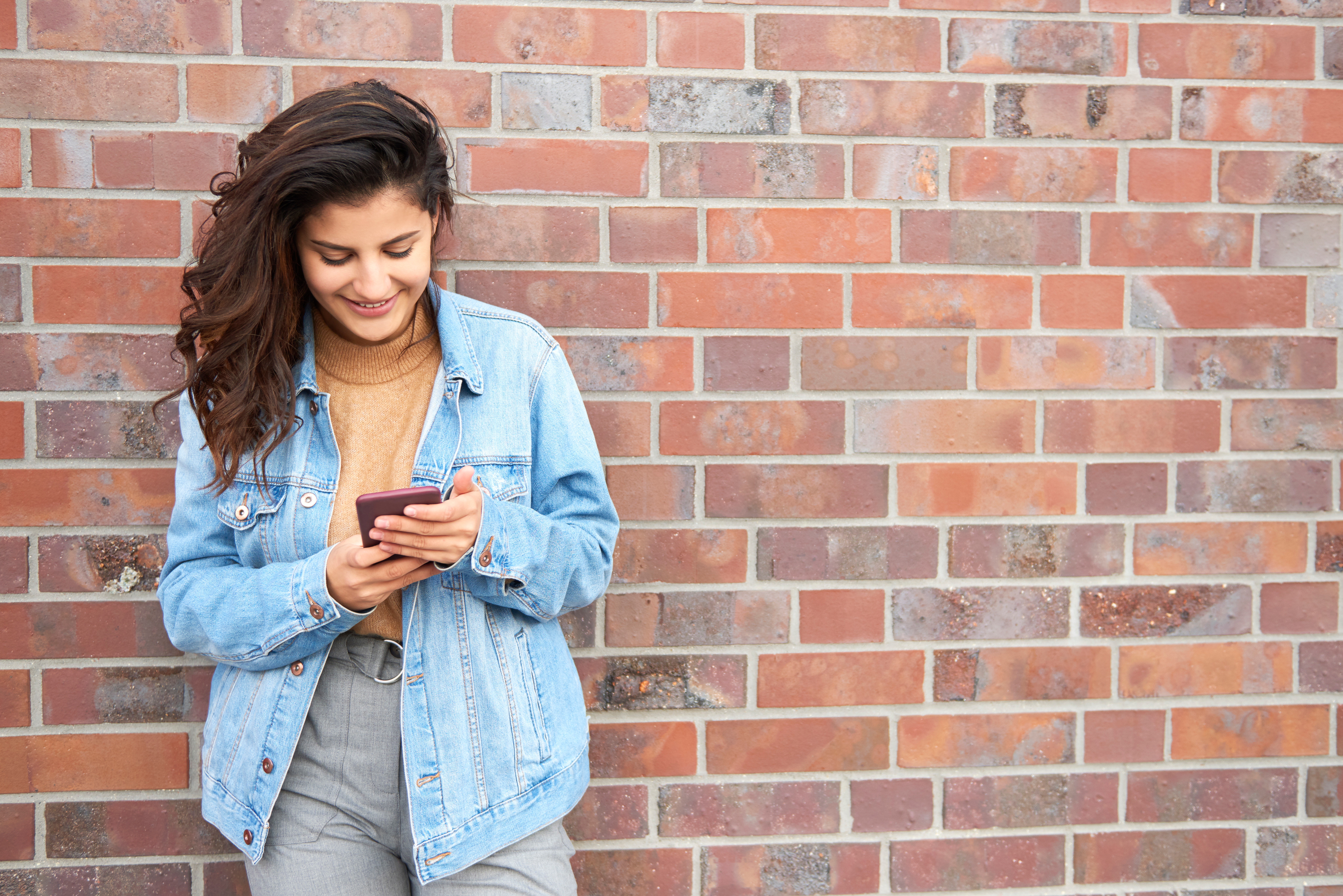 A girl in front of a brick wall looking at her phone