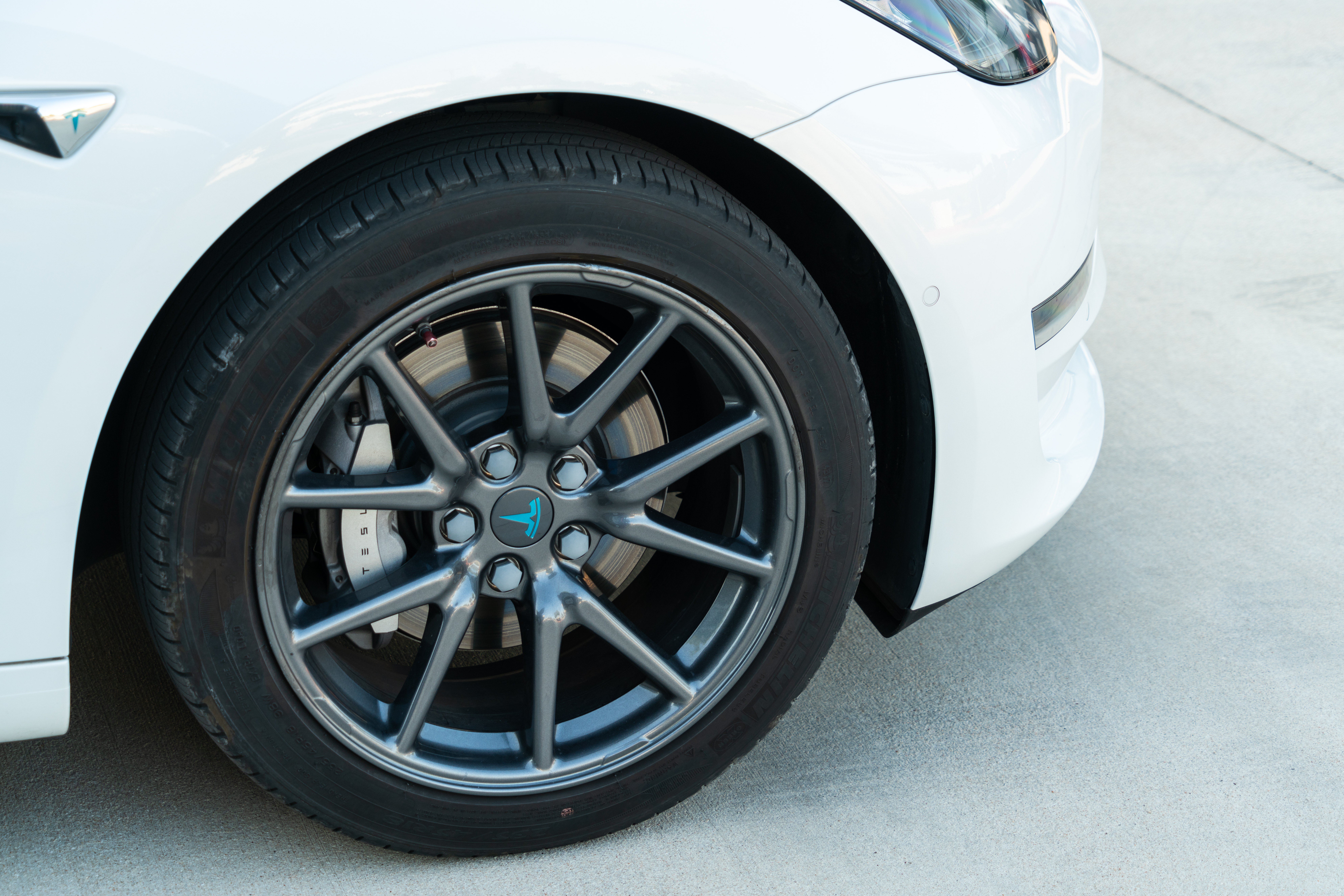 Blue Tesla Logo Inside a Performance Gun Metal Colored Rim and Michelin Performance Tire on a Tesla
