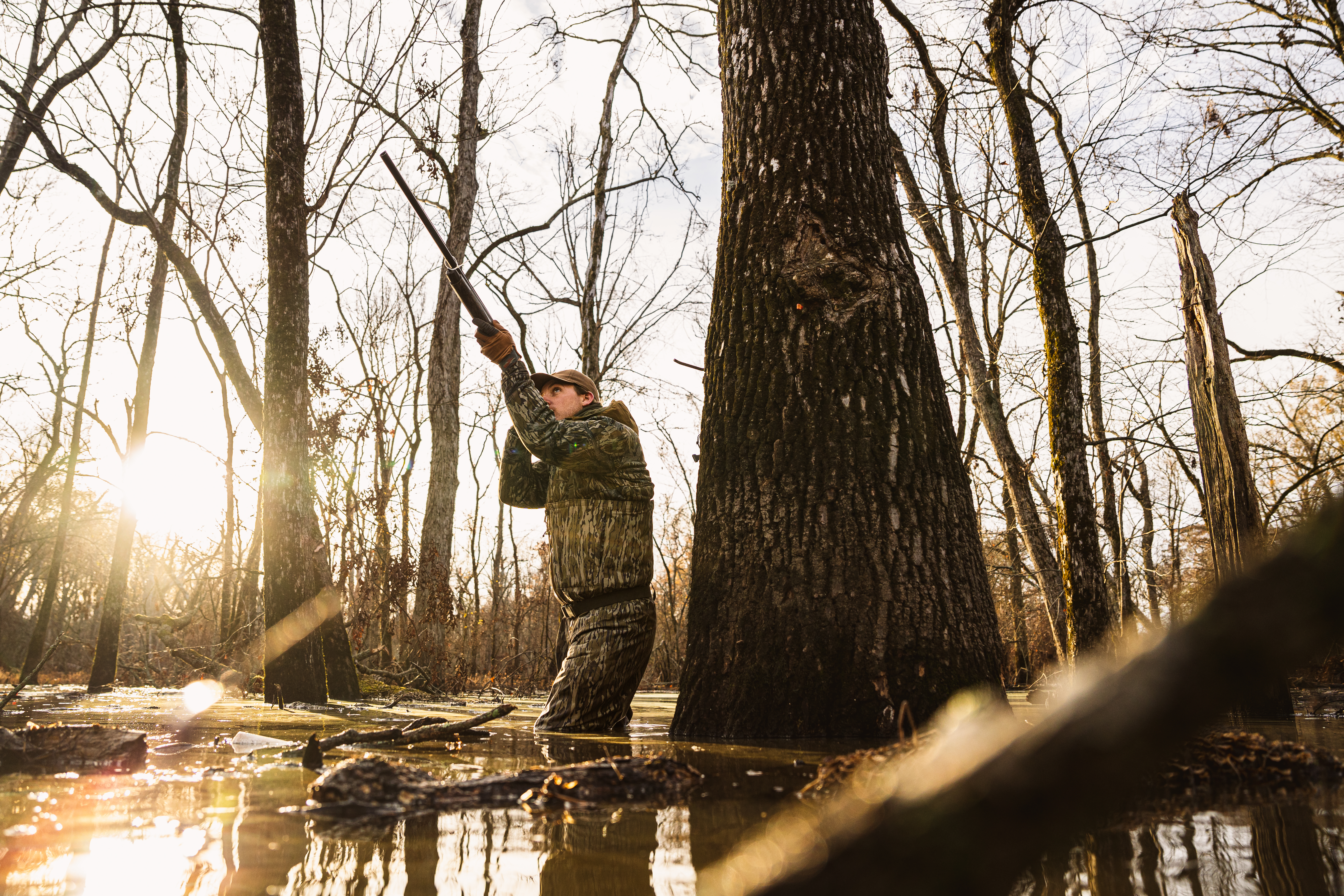 Duck hunter standing in flooded timber with a mounted gun