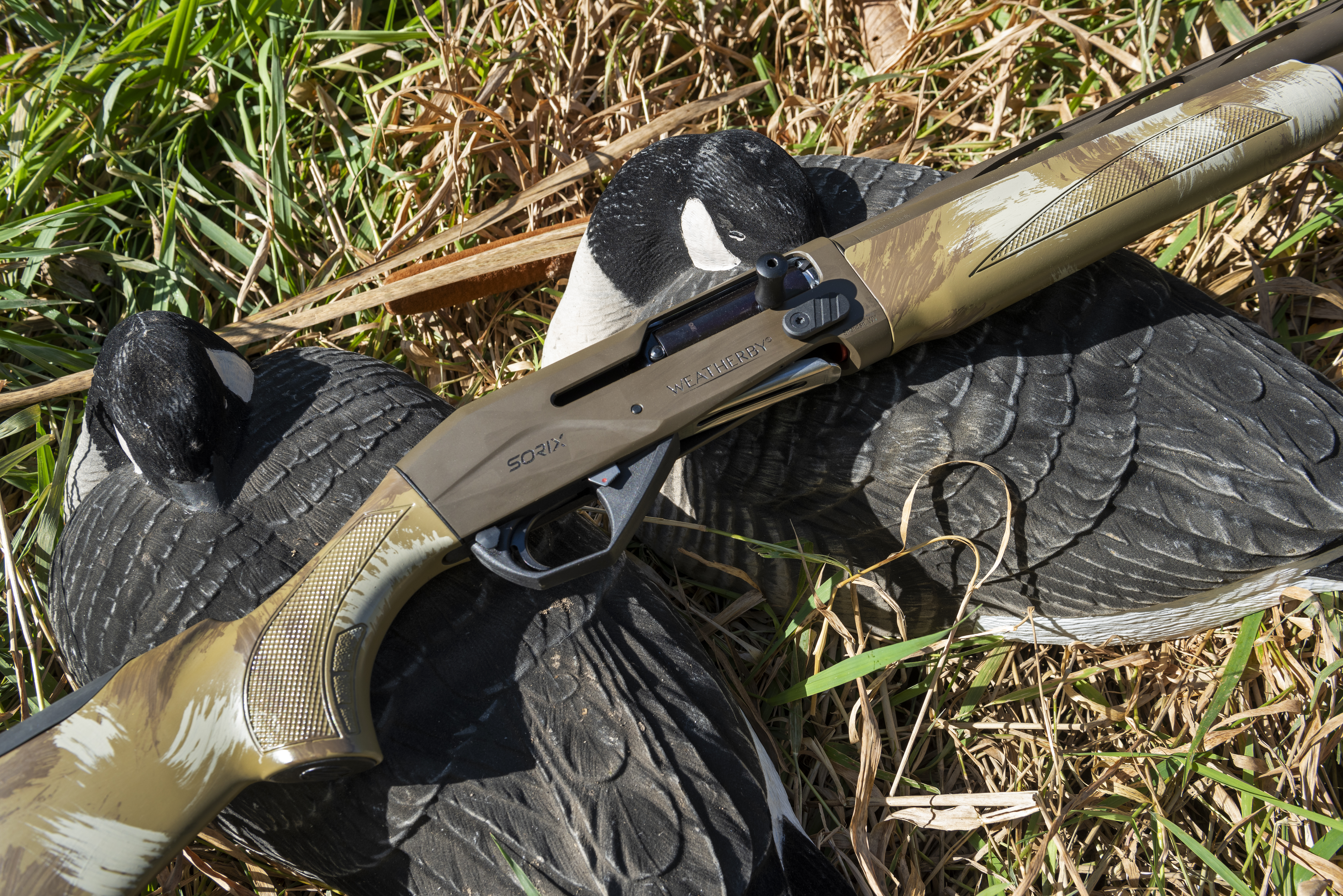 The new Weatherby Sorix shotgun lying on the grass with goose decoys. 