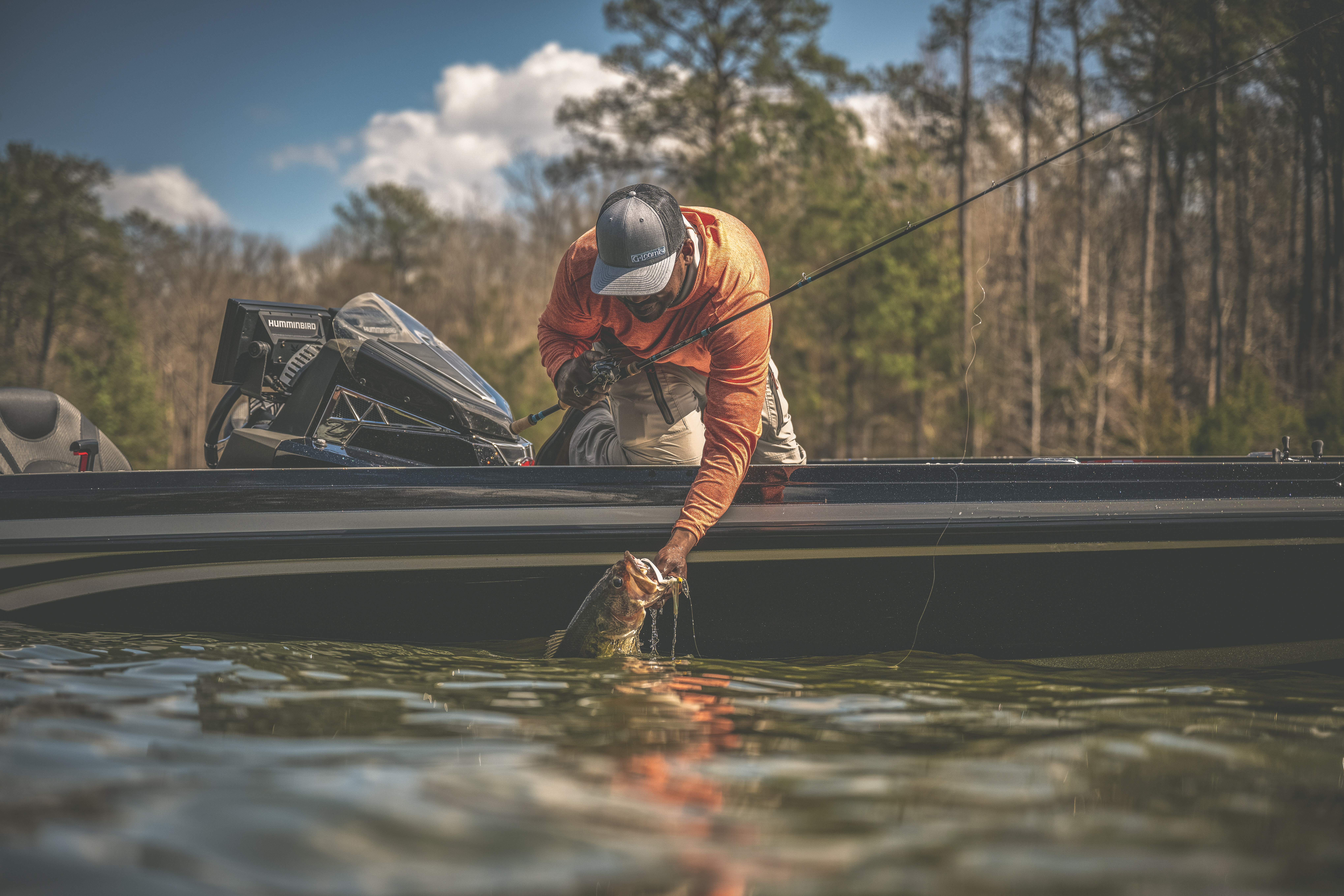 An angler in a boat reaches over to lip a big largemouth bass. 