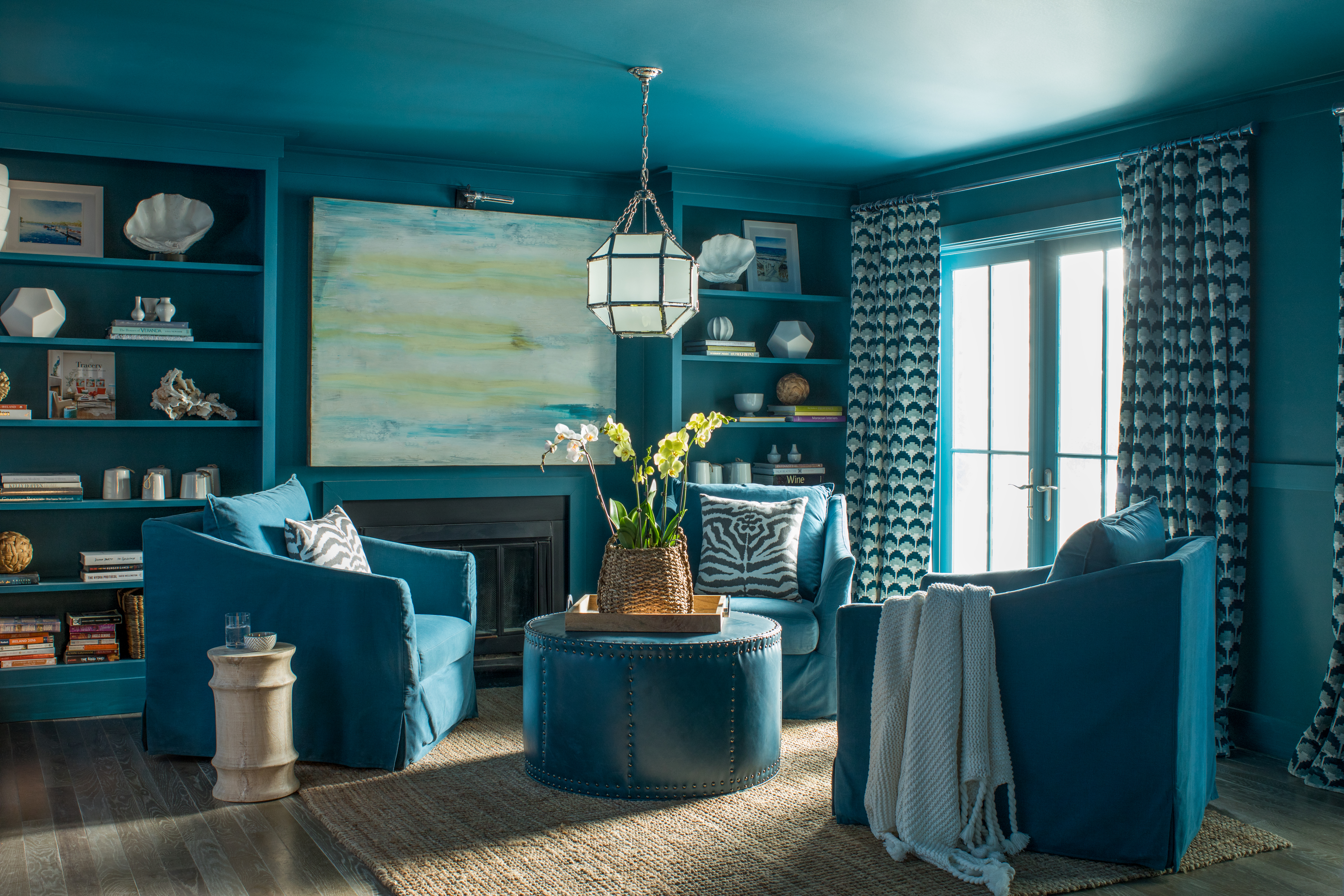 A living room displaying color drenching with blue armchairs, ottoman, blue bookcase, walls and ceiling