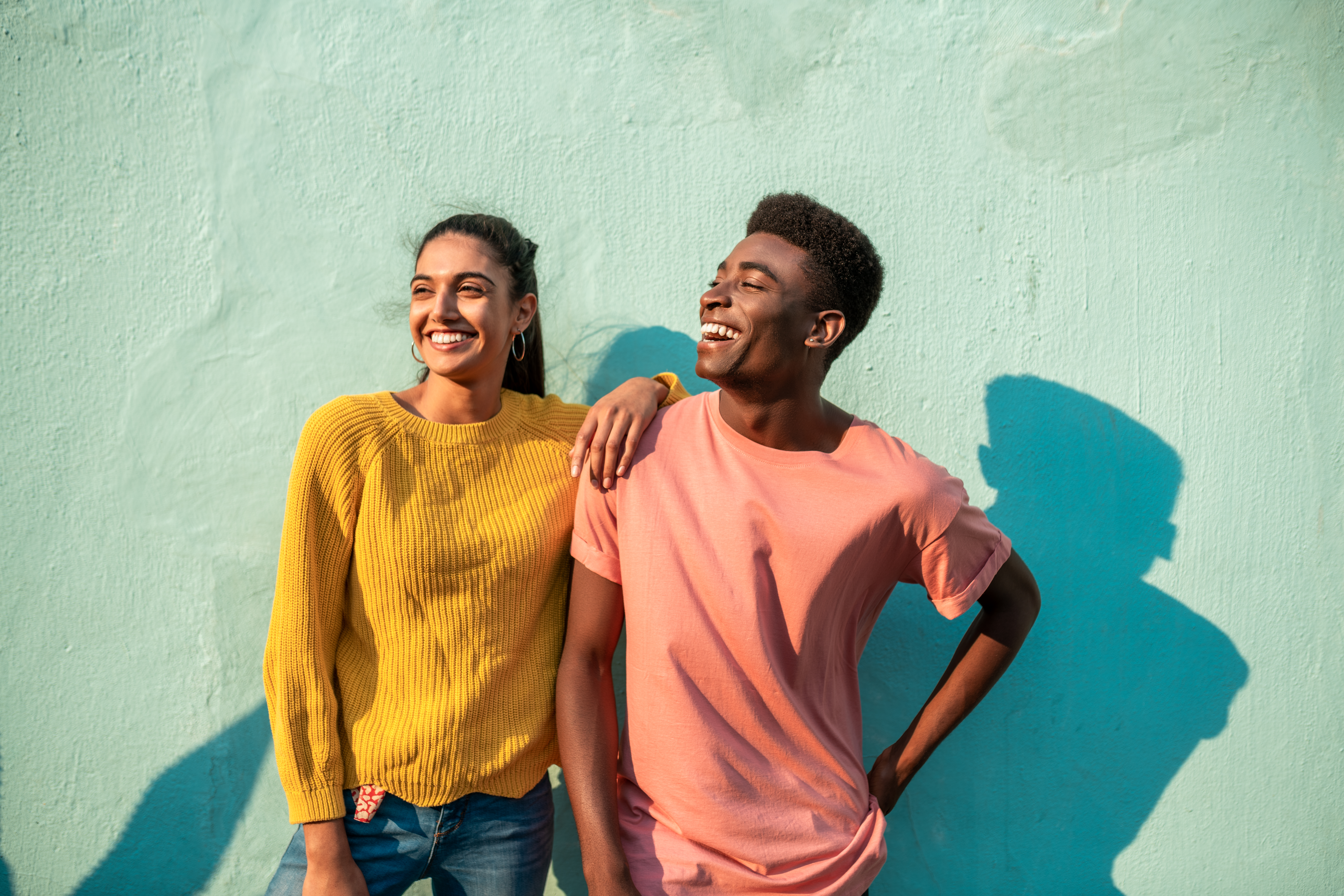 Two happy young adults, one woman/female and one male/man, looking to the left smiling with a green-blue background. landscape. iStock-1232764960