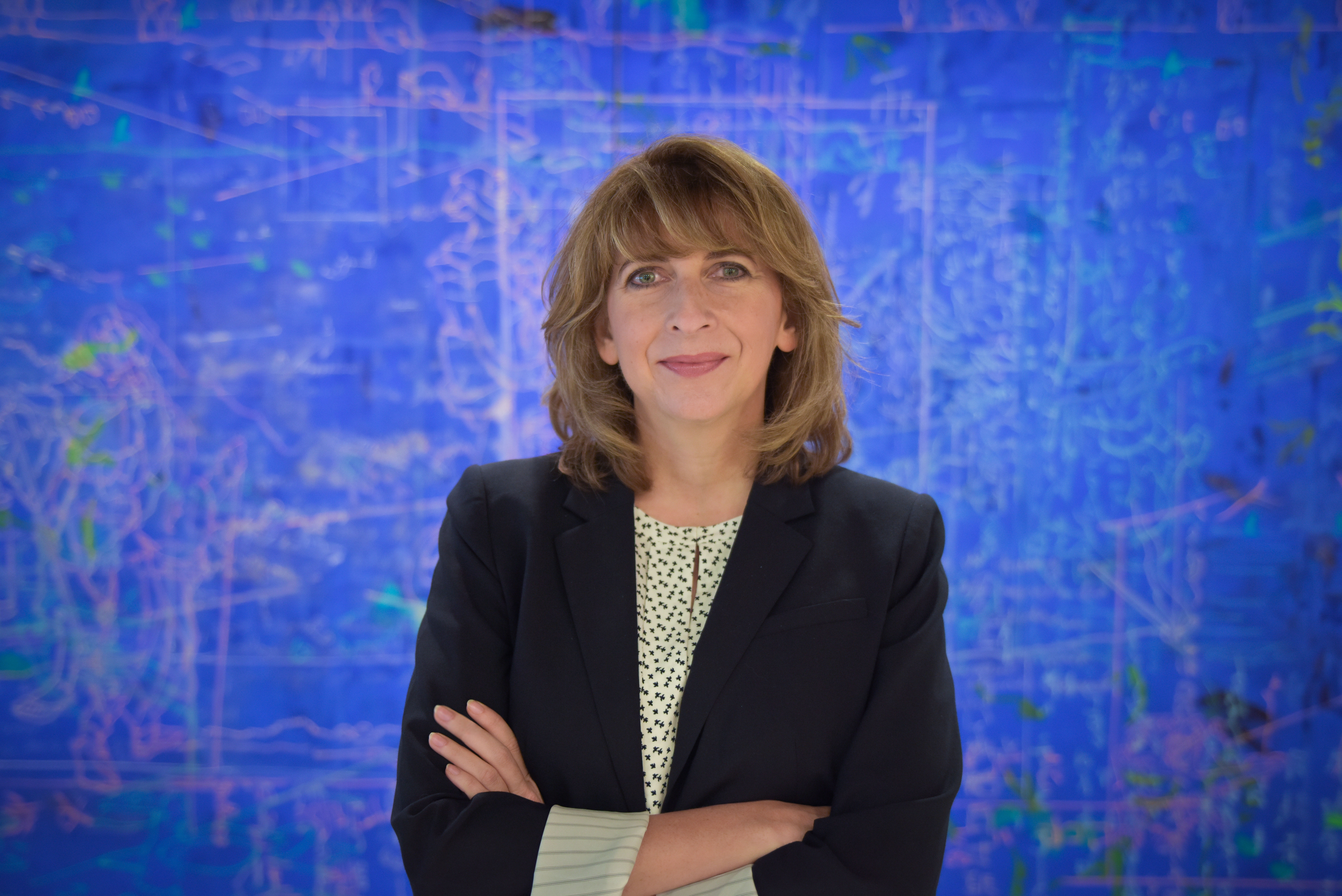 Leanne Young, CEO and executive director of The University of Texas at Dallas’ Brain Performance Institute, poses in front of a blue backdrop with her arms crossed.