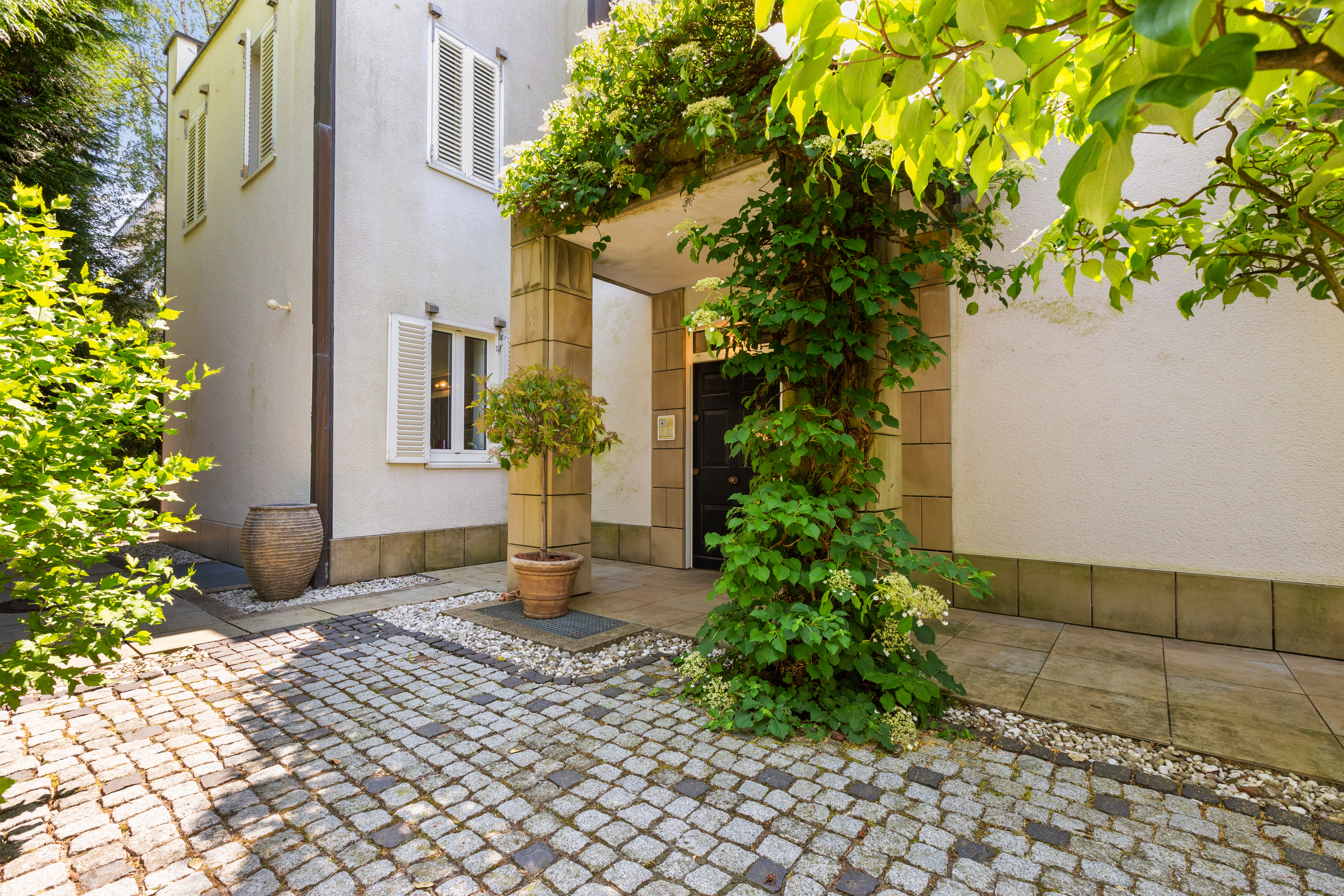 Eingang eines Wohnhauses mit Kletterpflanzen und Kopfsteinpflaster im Vorgarten.