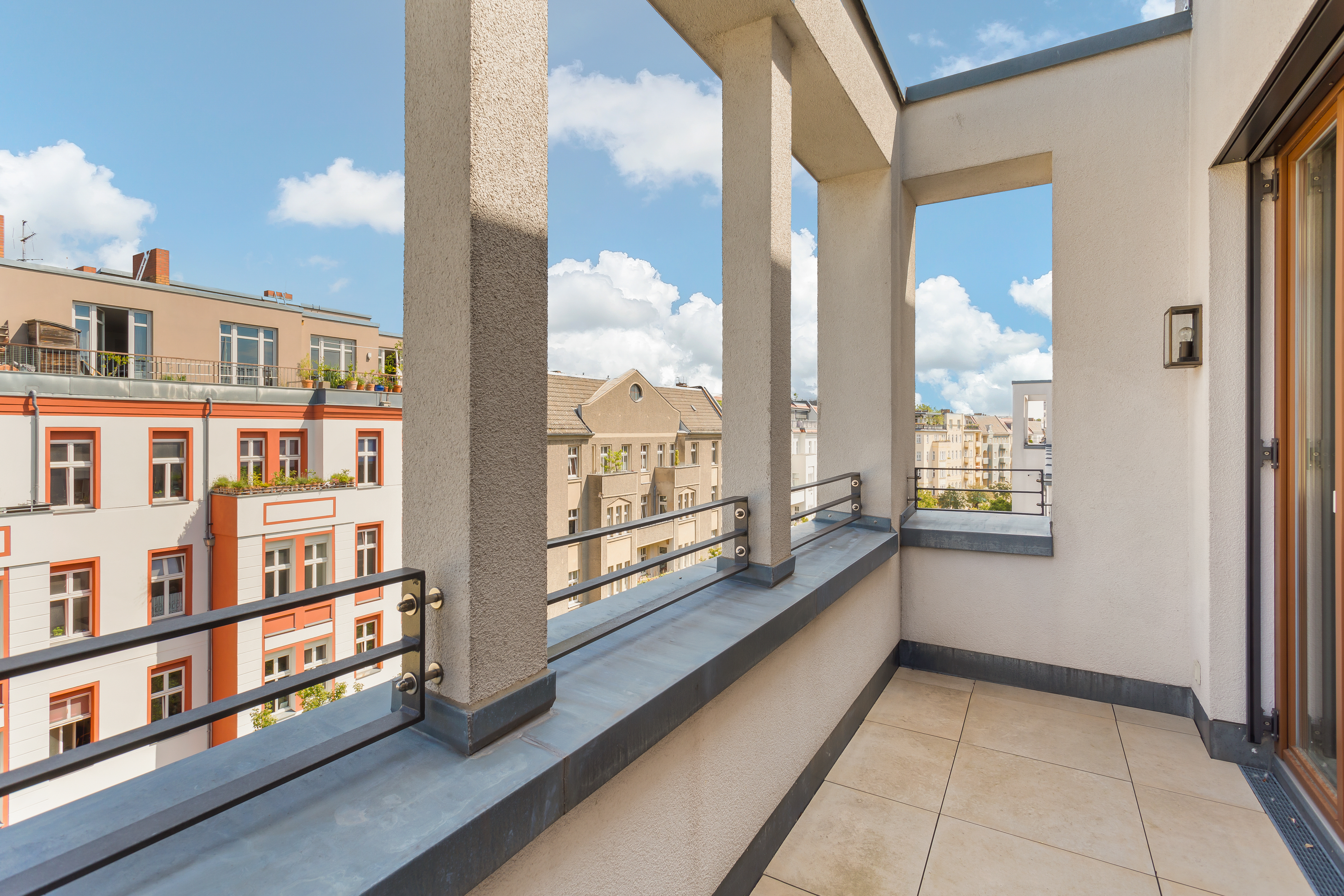 Überdachter Balkon mit Fliesen und Blick auf umliegende Wohnhäuser bei Sonnenschein.