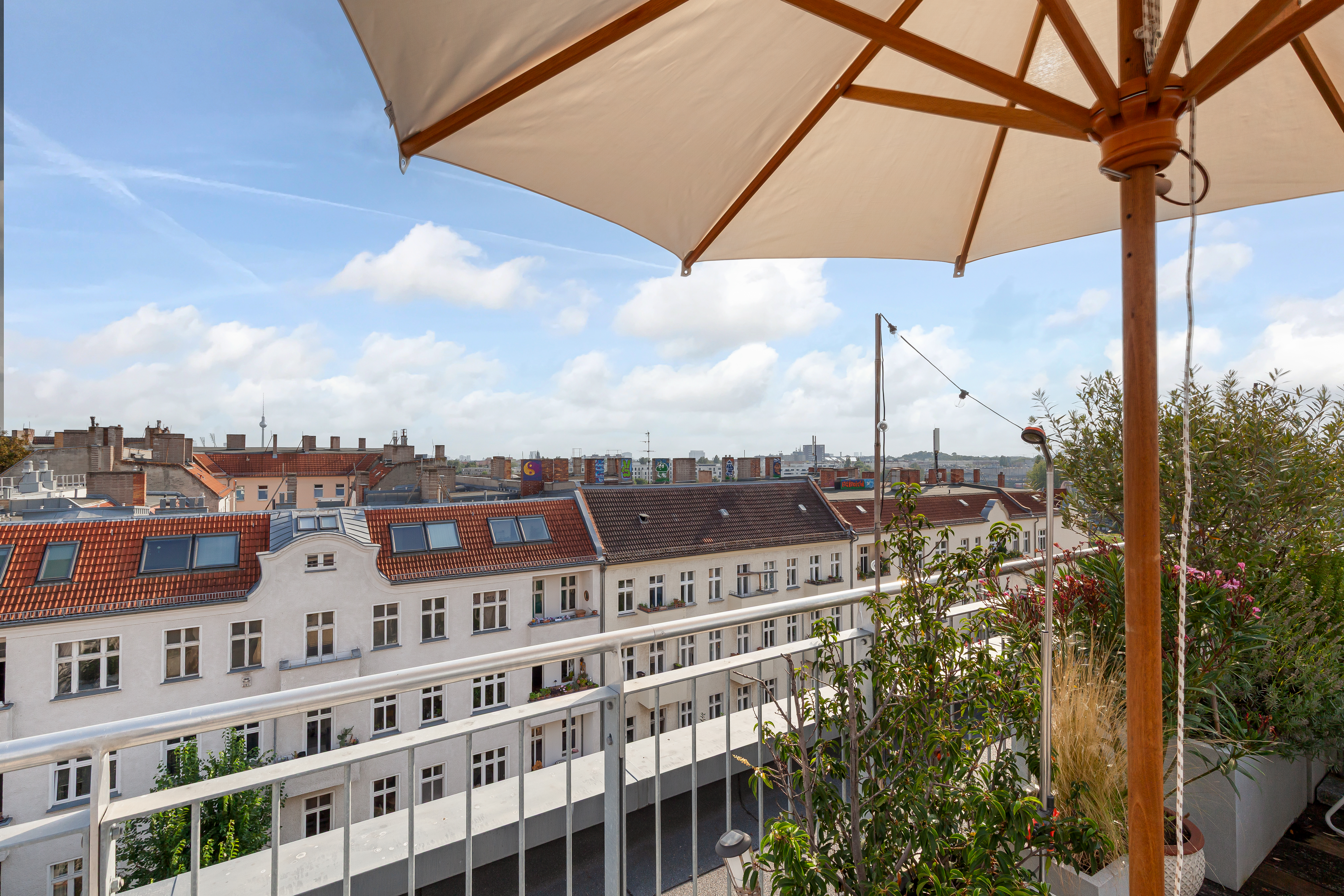 Balkon mit Sonnenschirm, Pflanzen und Blick auf rote Hausdächer.
