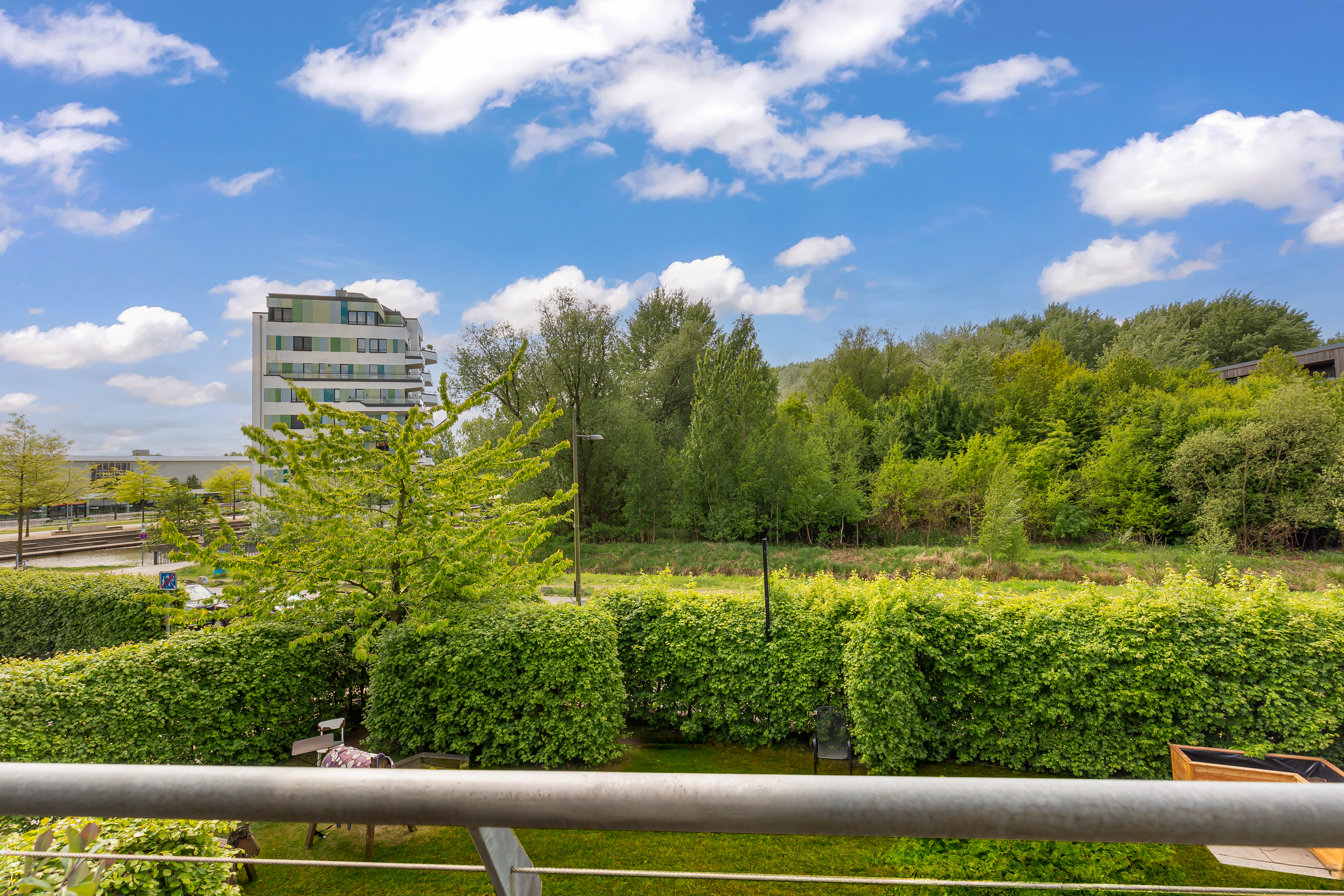 Blick von einem Balkon auf Garten, Bäume und ein modernes Wohngebäude im Hintergrund.