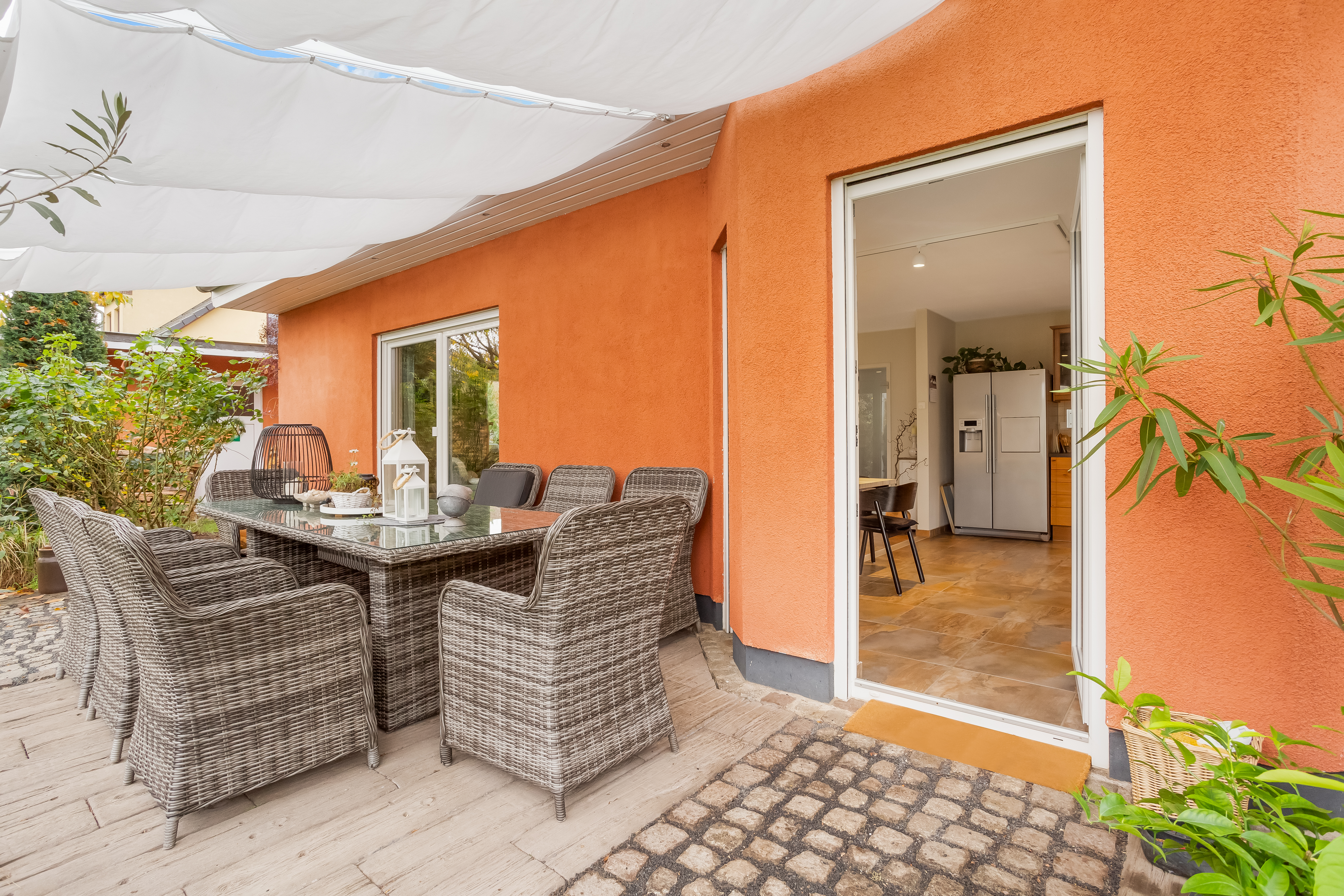 Überdachte Terrasse mit Rattansitzgruppe und Blick in eine Küche mit großem Kühlschrank.