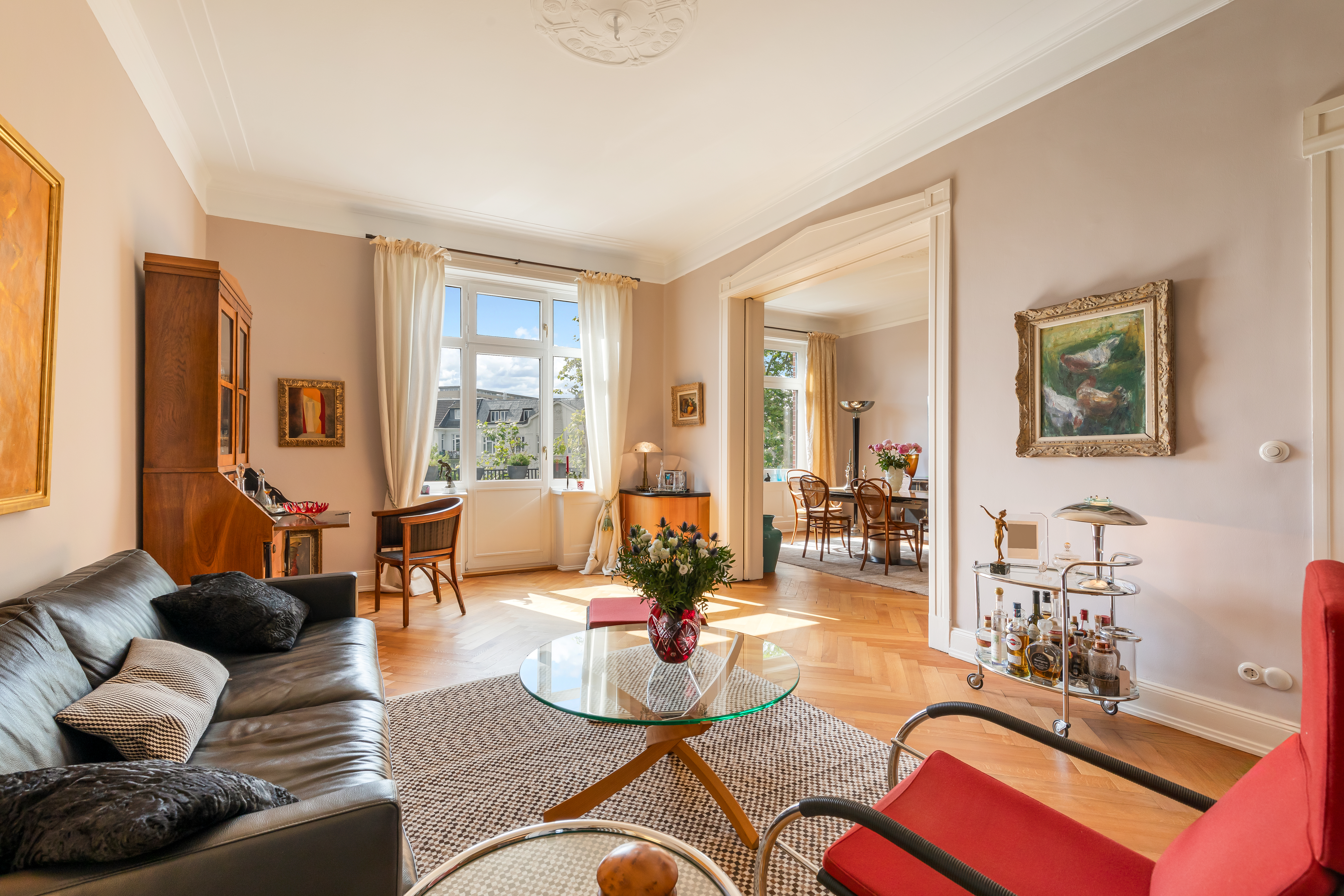 Helles Wohnzimmer mit Ledersofa, Glastisch, Schreibtisch am Fenster und Blick ins Esszimmer.