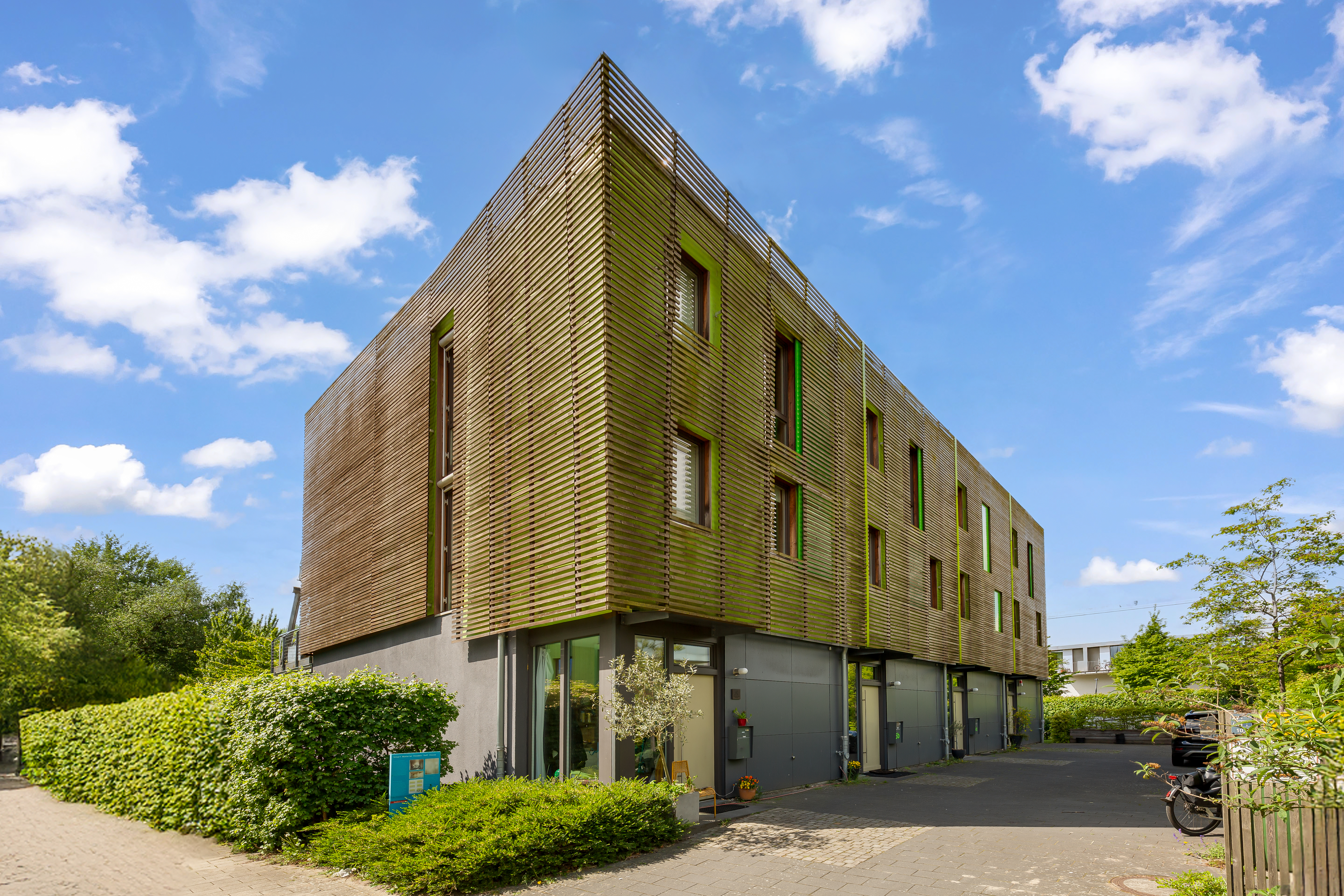 Modernes Wohngebäude mit Holzfassade und mehreren Fenstern, umgeben von viel Grün.