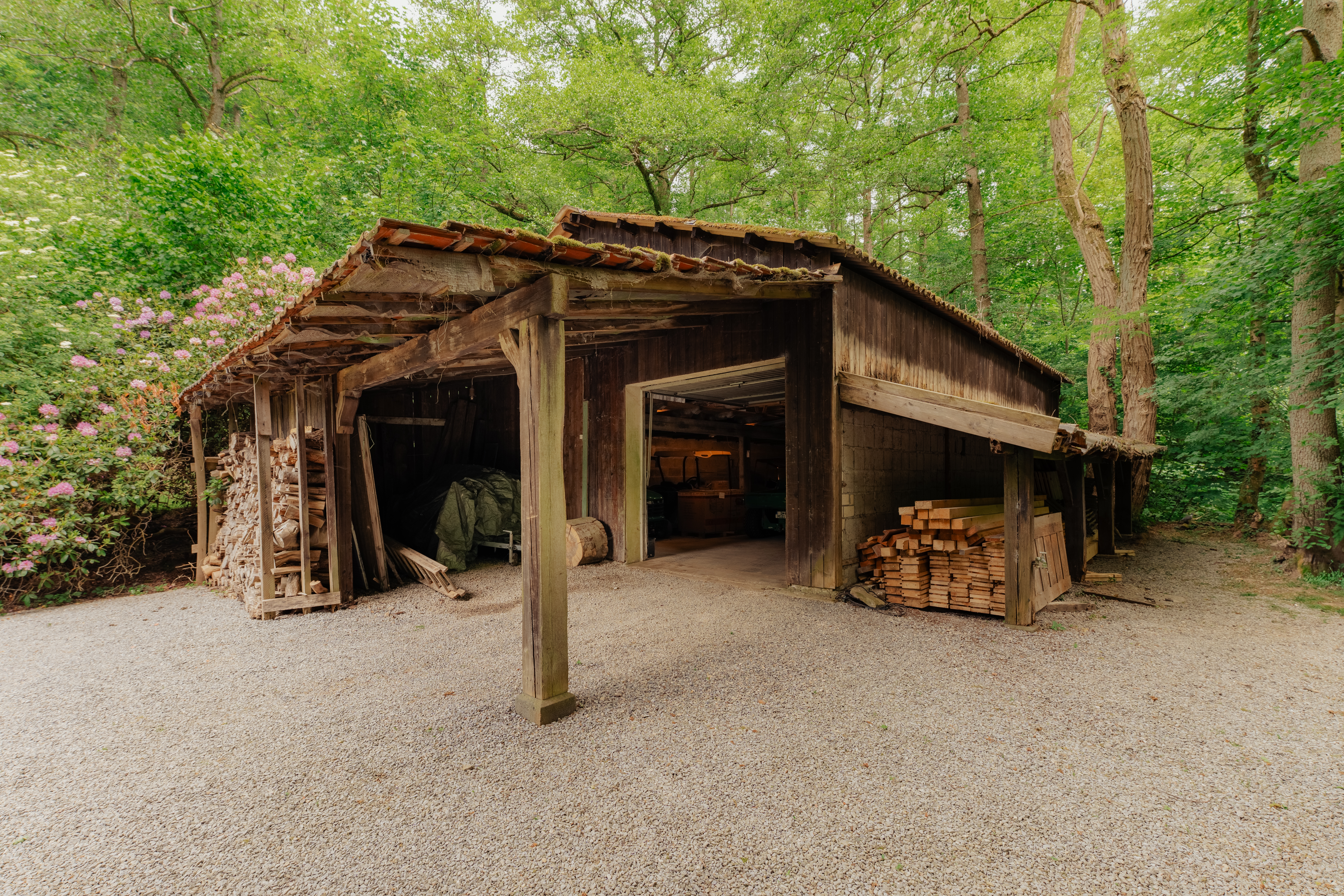 Alte Holzscheune mit gestapeltem Holz und offenen Seiten im Grünen.