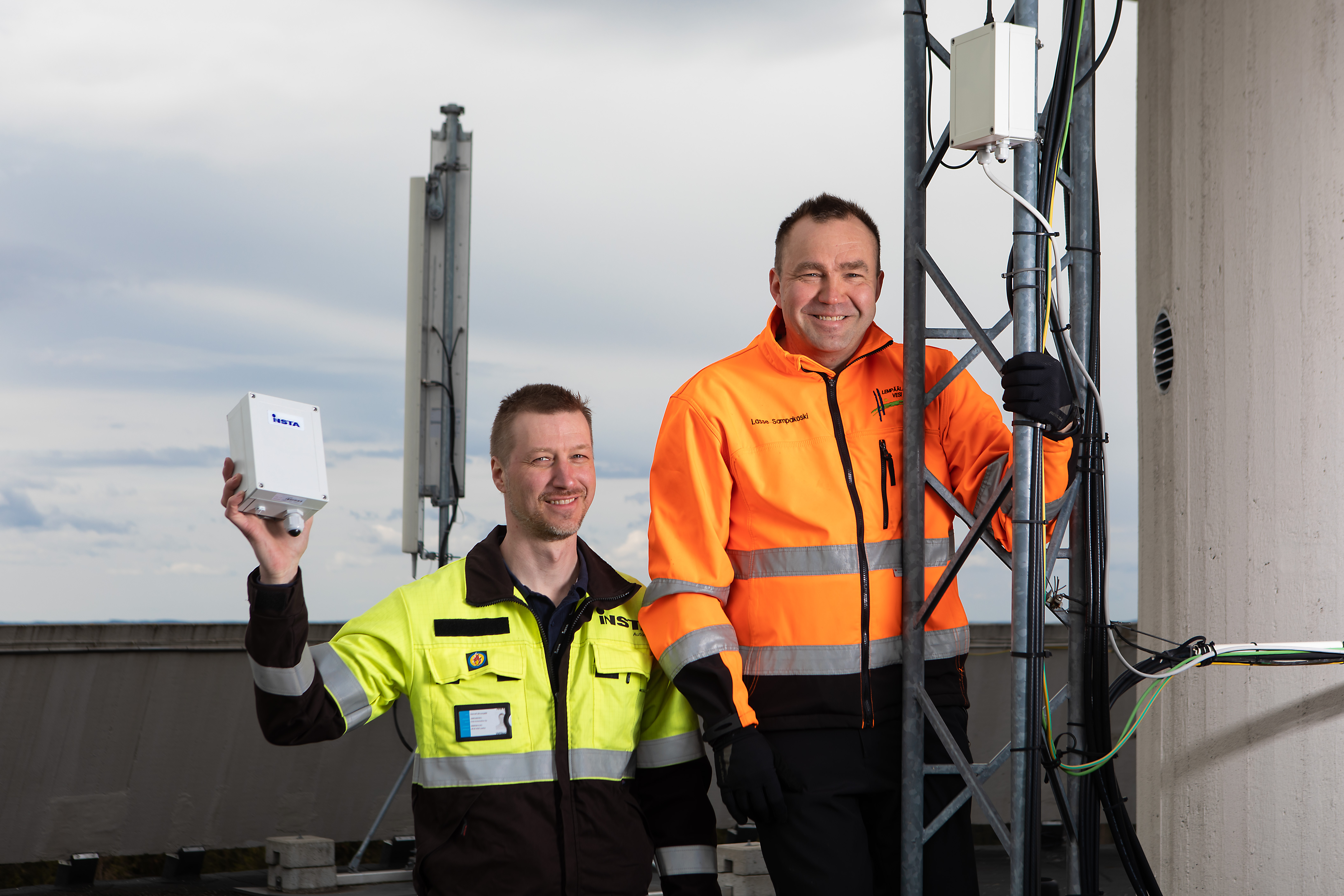 An Insta employee and a customer are standing on top of the water tower, posing with the Insta Wave measurement solution.