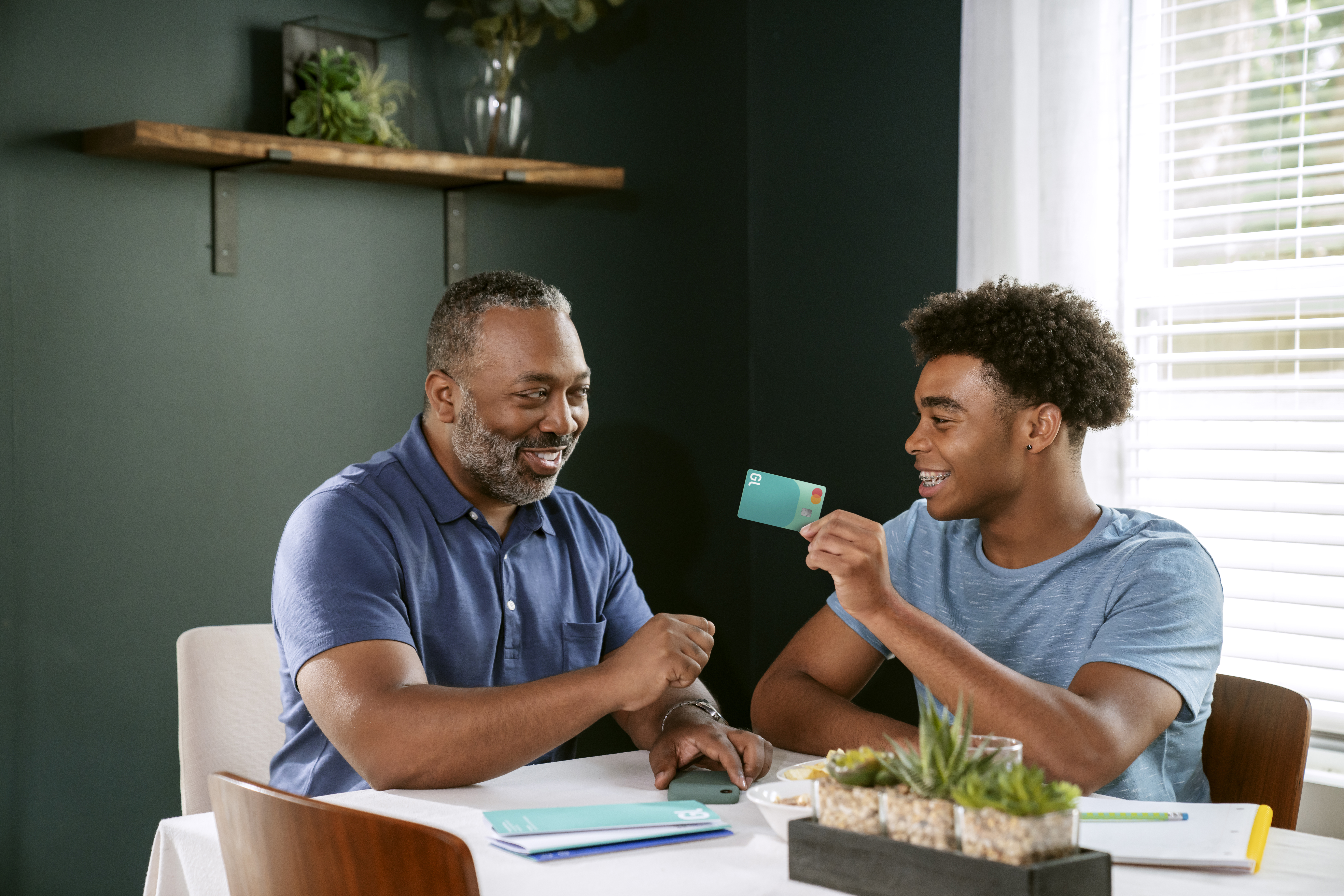 Father and son sit at dinner table talking about checking vs. savings accounts