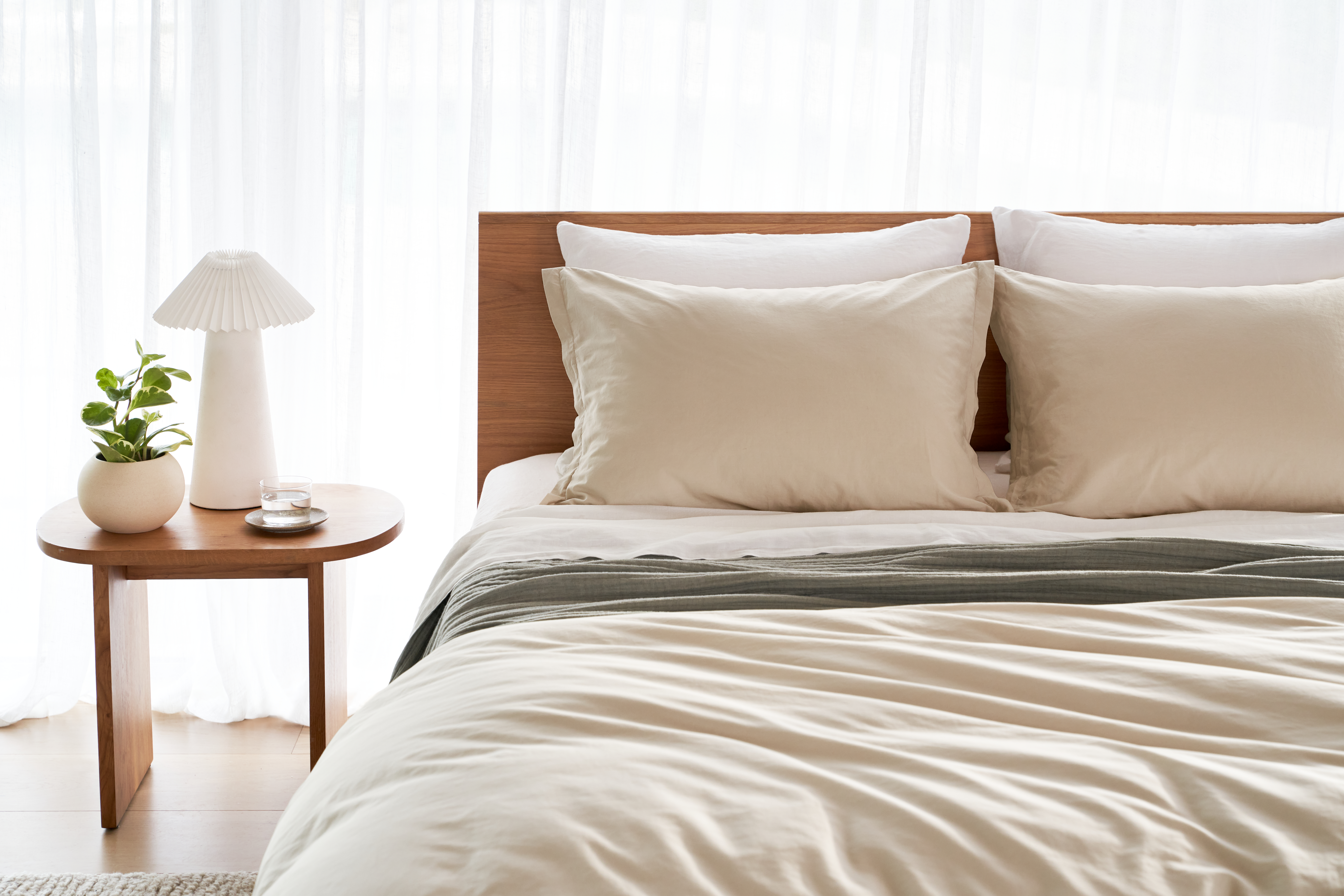 Close up image of neutral colored percale sheeting on a bed in a bright bedroom