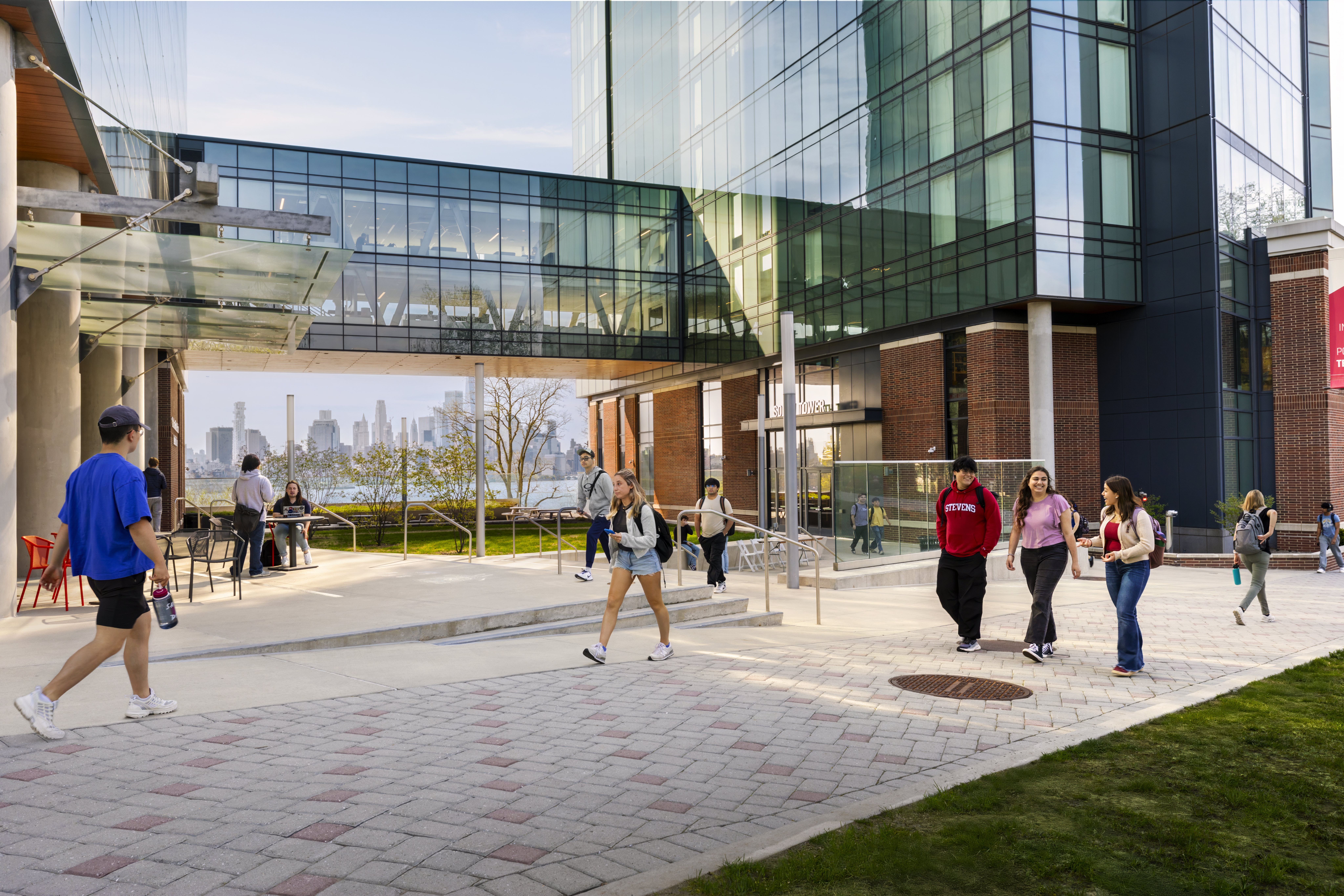 Students walk on a pathway upon Stevens campus with New York City skyline in the background.