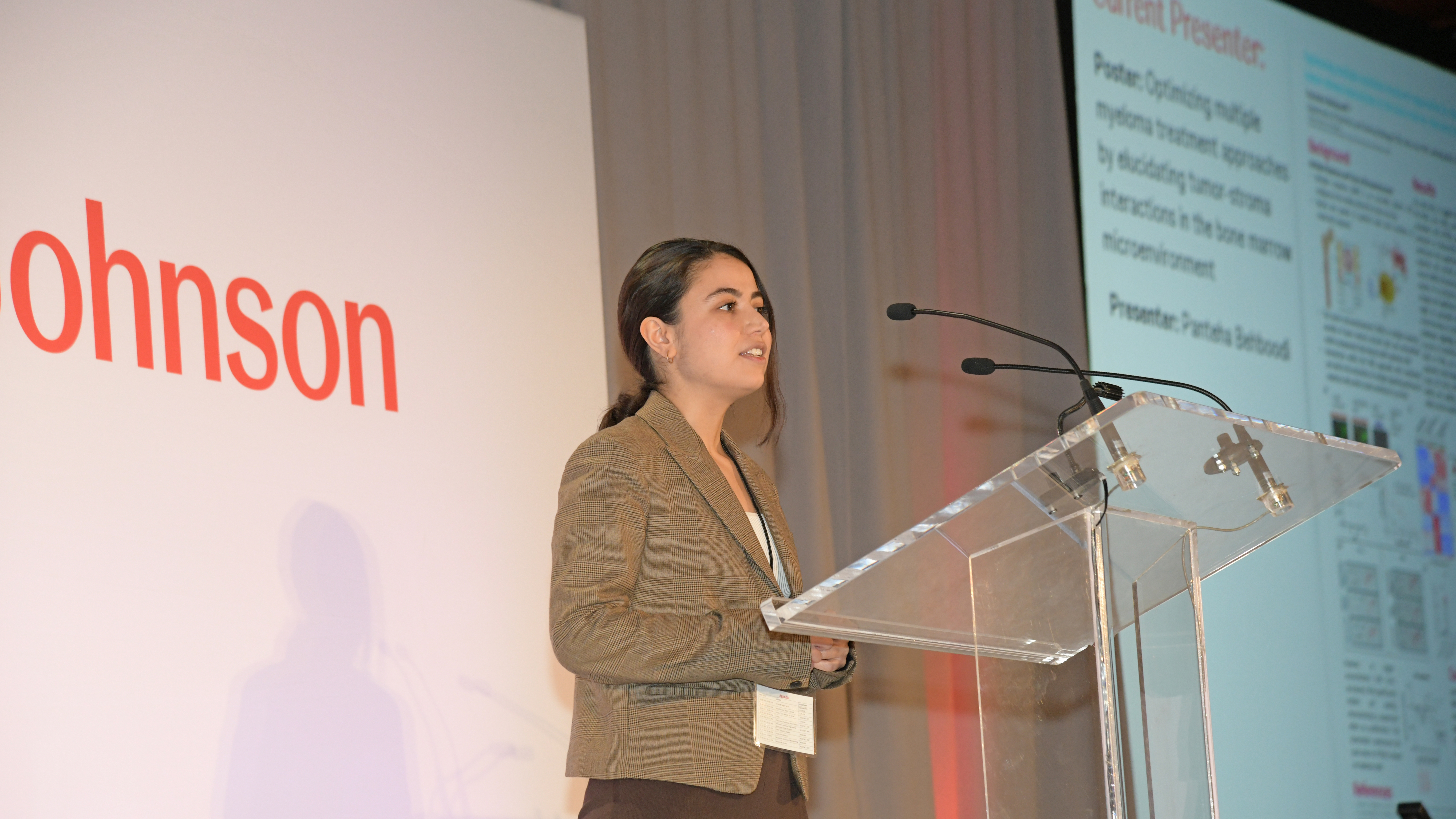 Student Panteha Behboodi stands speaking behind a podium with the Johnson & Johnson logo in the background.