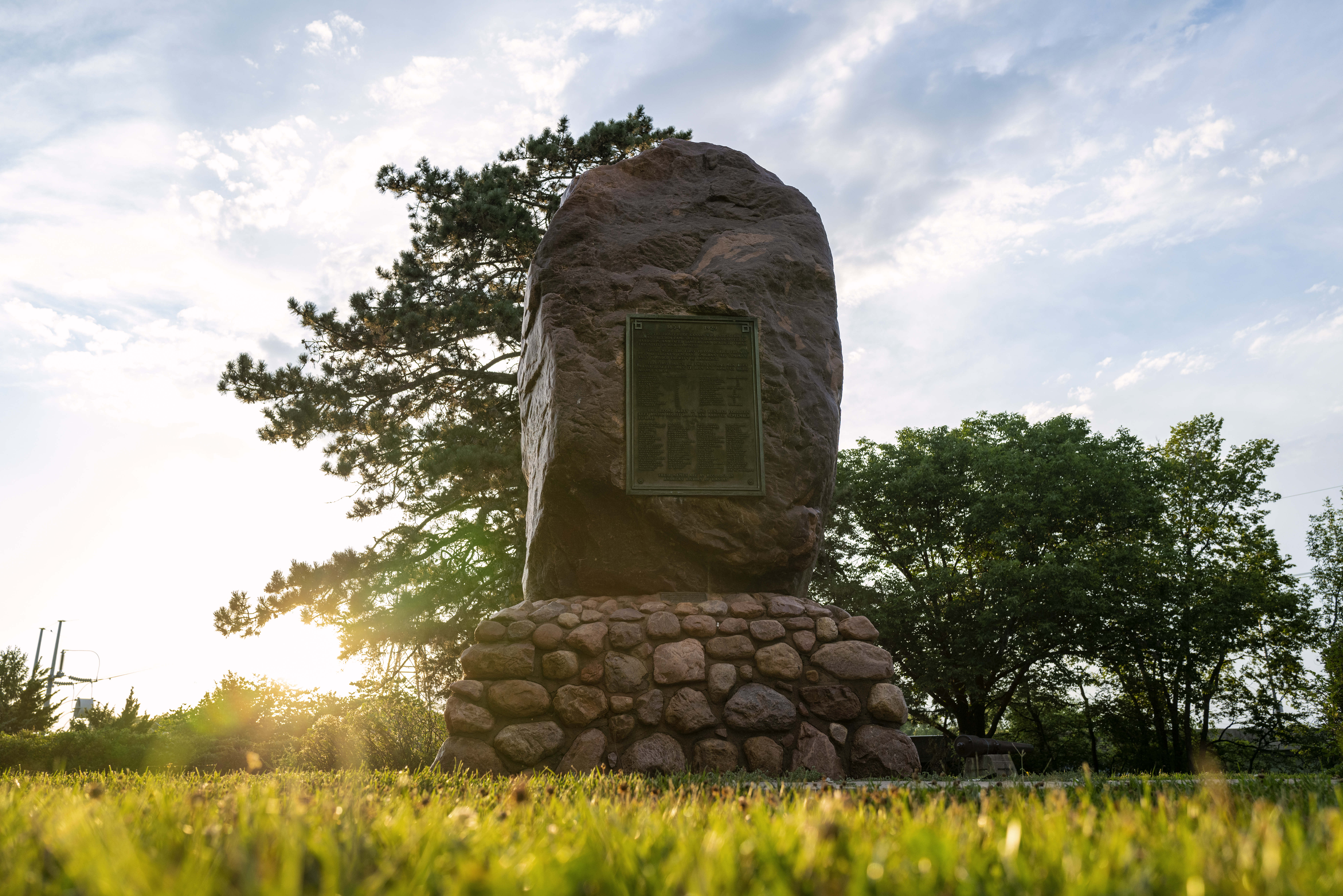 In a clearing at sunrise, a tall red stone boulder sits on a pedestal made of smaller stones. The boulder is almost as tall as the trees around it.