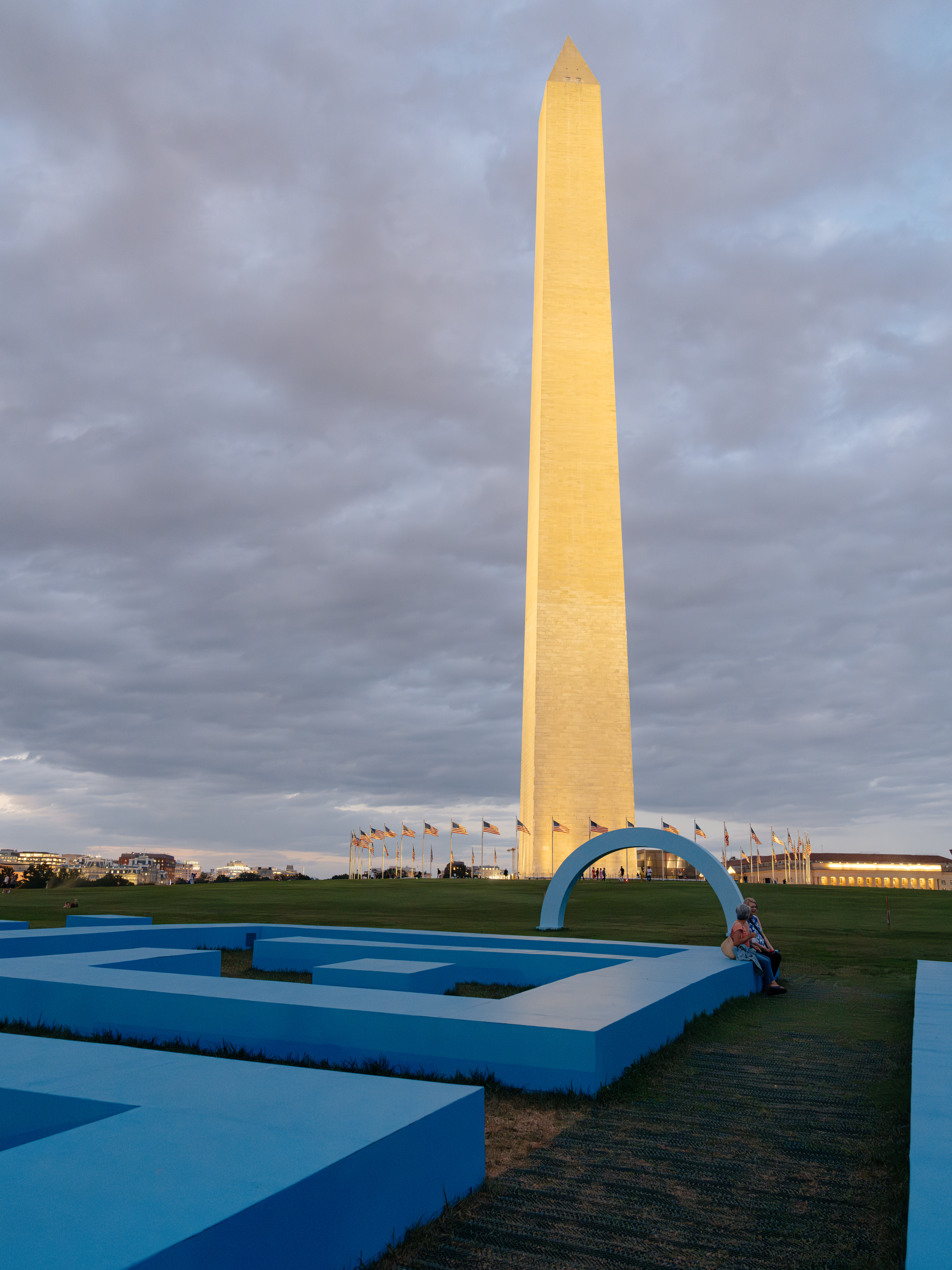 The Washington Monument at sunset overlooking a group of blue sculptures sitting on the ground beneath it