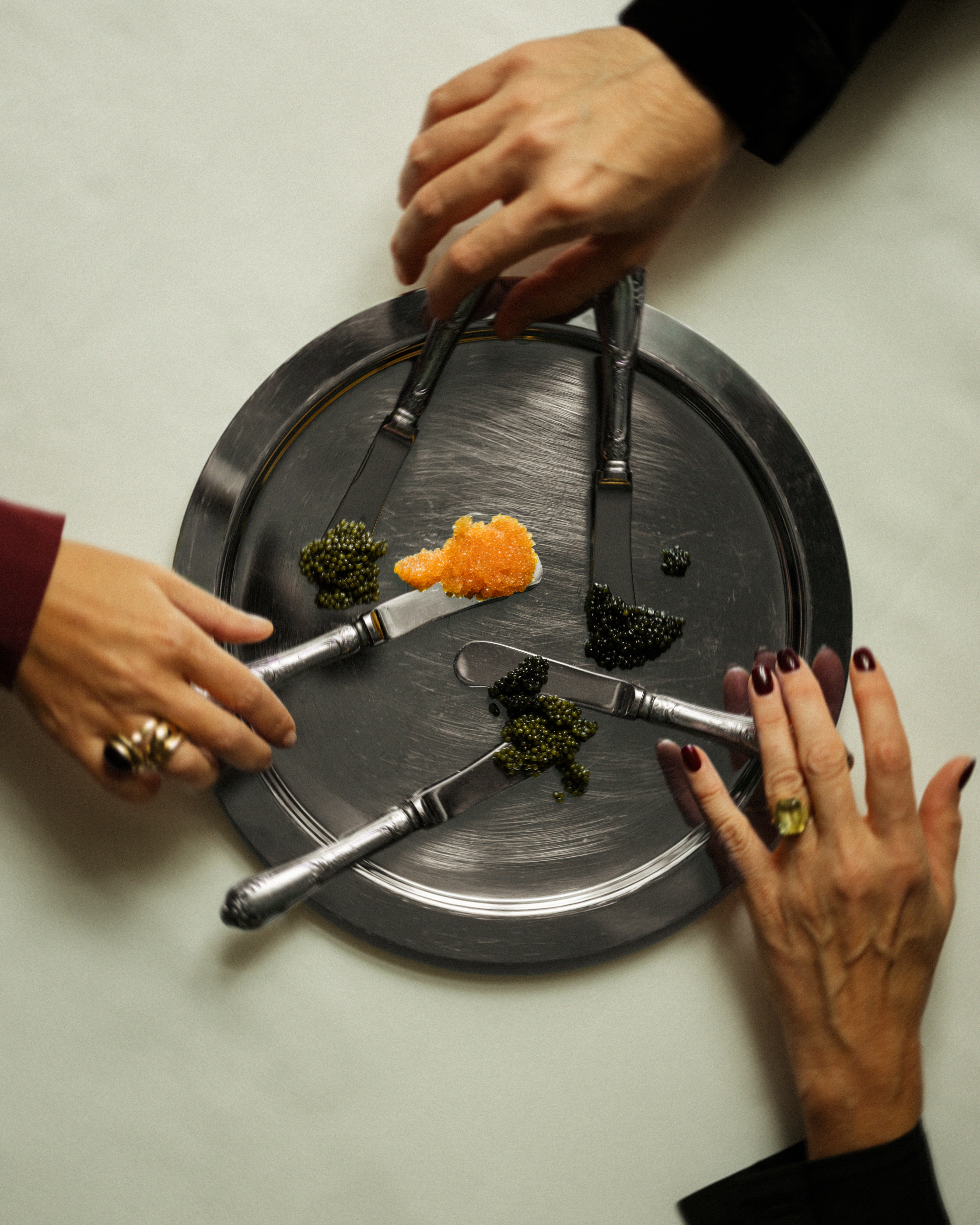 Hotel Kämp – À La Kämp. Kädet kurkottavat hopeatarjottimelle, jossa on erilaisia kaviaareja ja tarjoiluveitsiä, valmiina nautittavaksi.