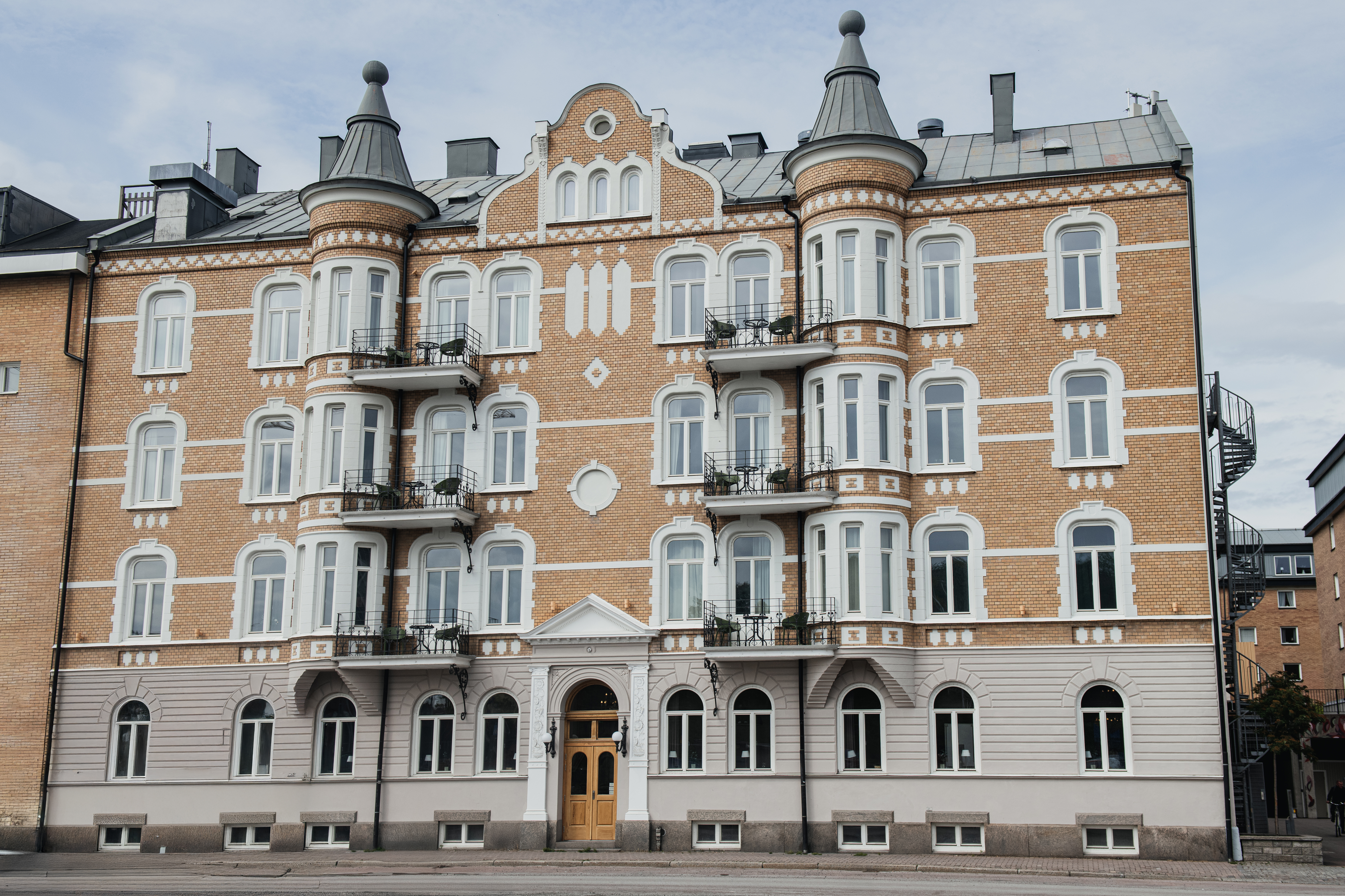 En rikt utsmyckad fyravåningsbyggnad med rundade torn och flera fönster visar en klassisk arkitektur. Balkonger på varje våning är försedda med räcken, i en stadsmiljö.