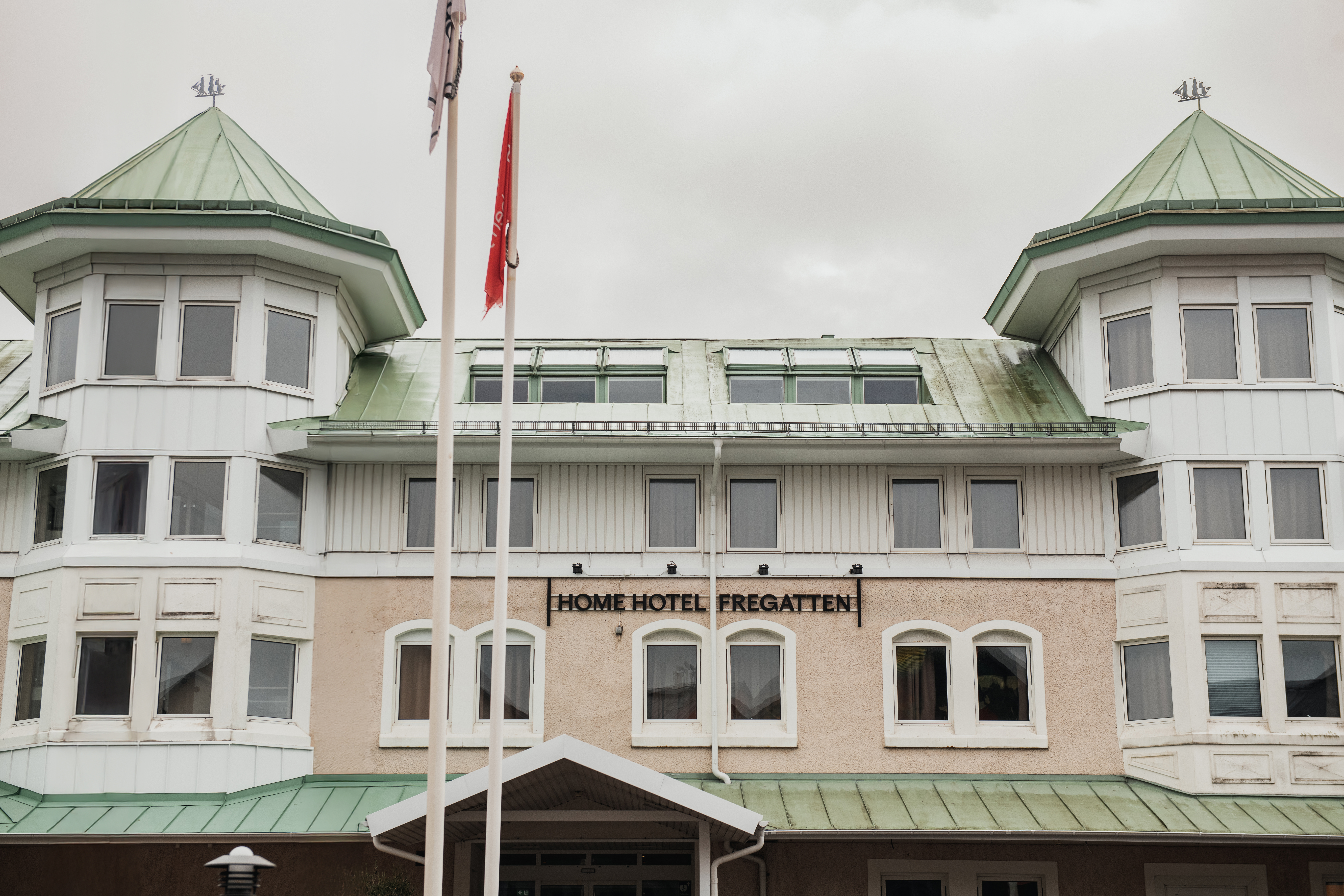 Udvendig udsigt over en hotelbygning med grønne tage og karnapper. Et skilt på facaden læser HOME HOTEL FREGATTEN.