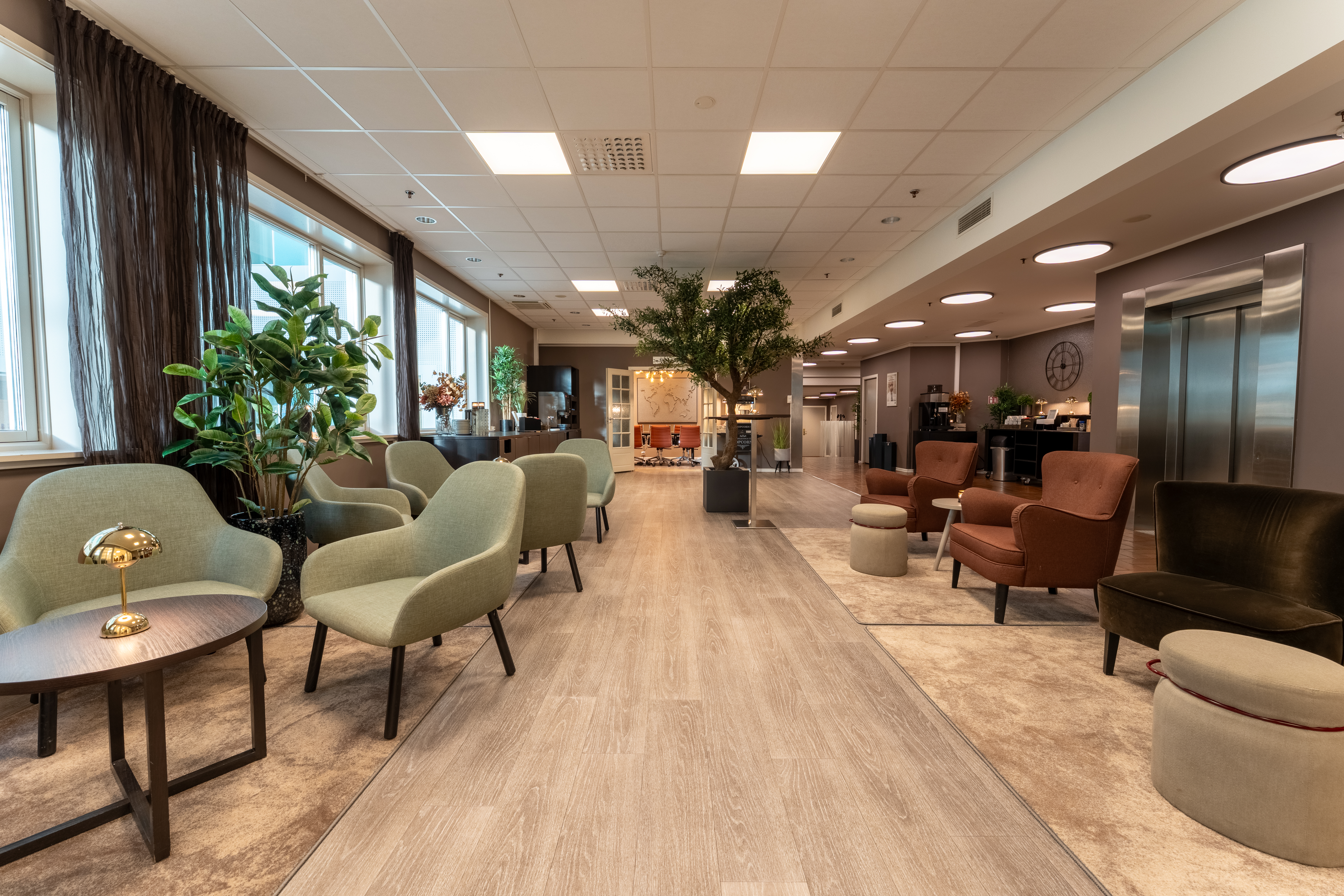 Kutsuva hotelliaula, jossa on mukavat istuinalueet, reheviä kasveja ja suuret ikkunat, kutsuen vieraat rentoutumaan.