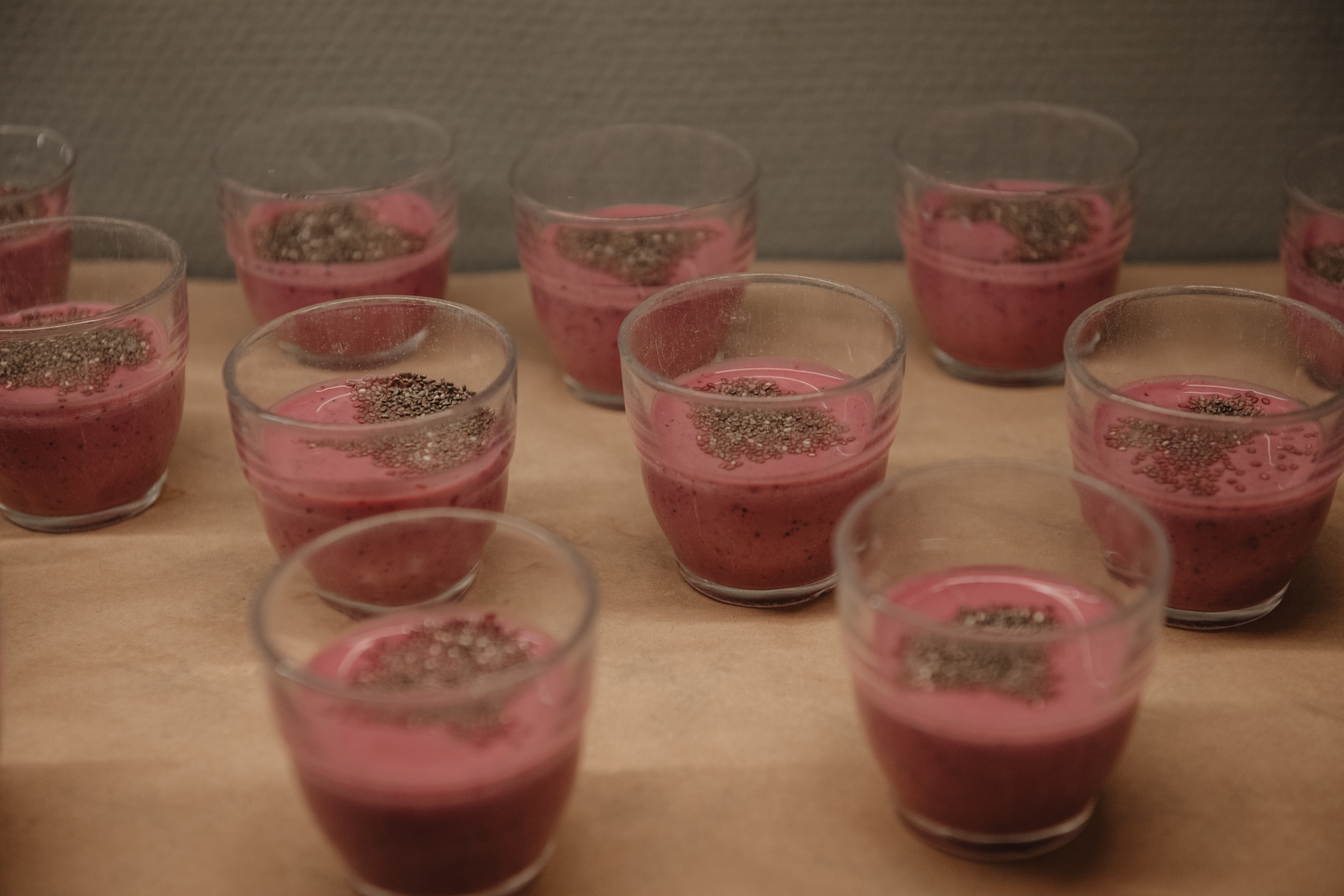 Flera små glas med rosa krämiga godsaker, garnerade med frön, redo att avnjutas.