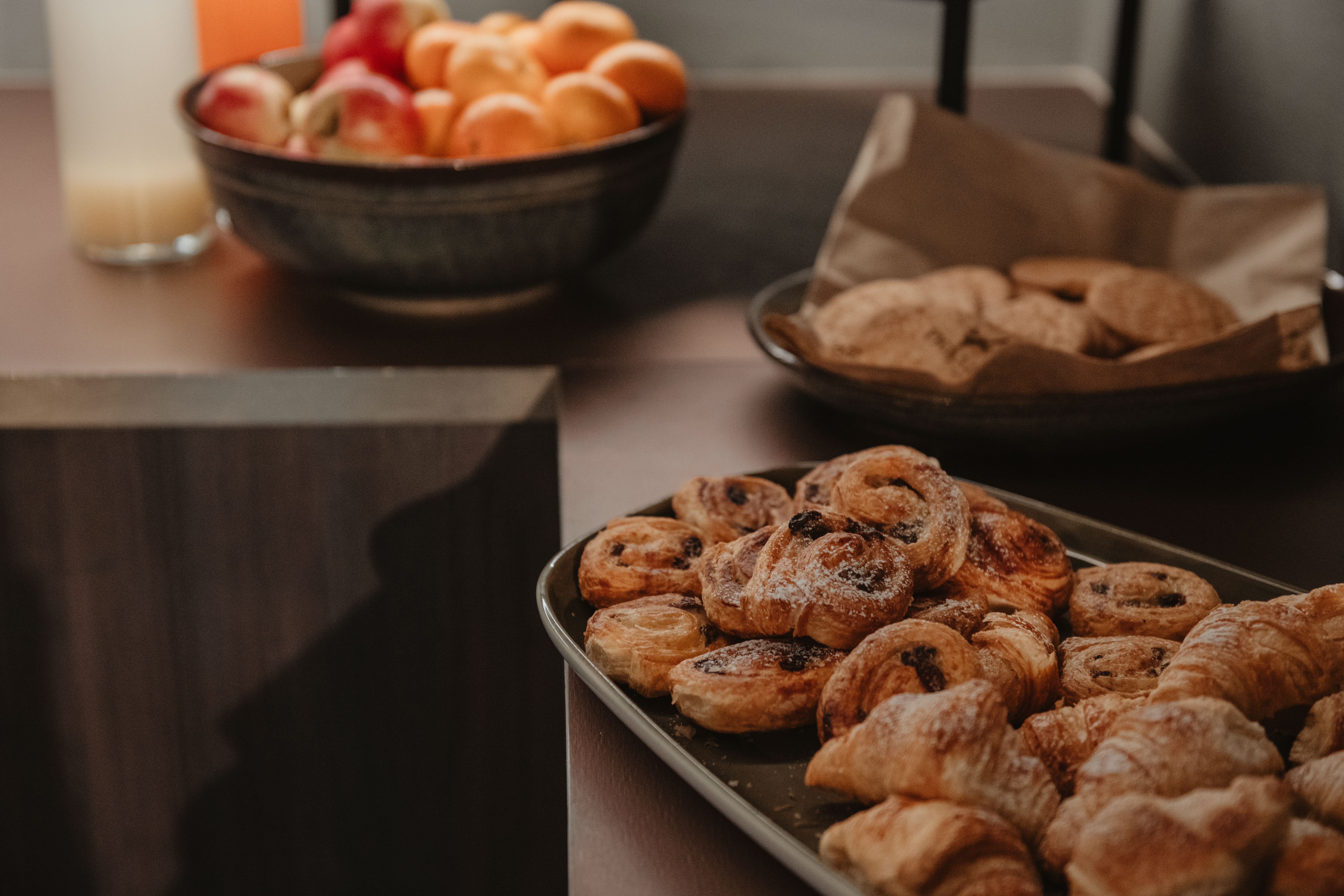 En frukostbuffé med en bricka nybakade bakverk, en skål färgglad frukt och ett glas juice.