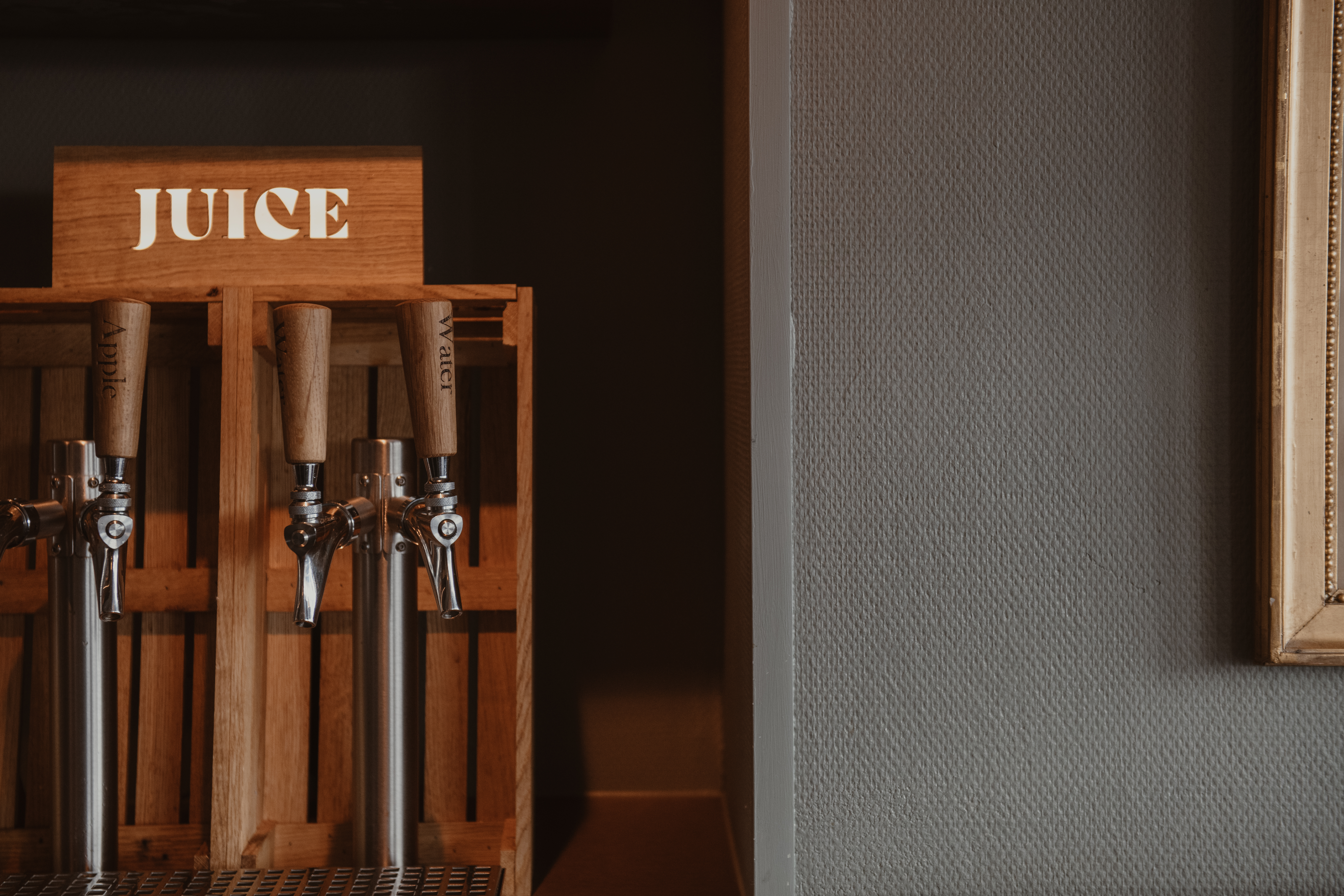 En självbetjäningsdryckesstation med tre kranar, som erbjuder JUICE, Äpple och Vatten från trädispensrar.