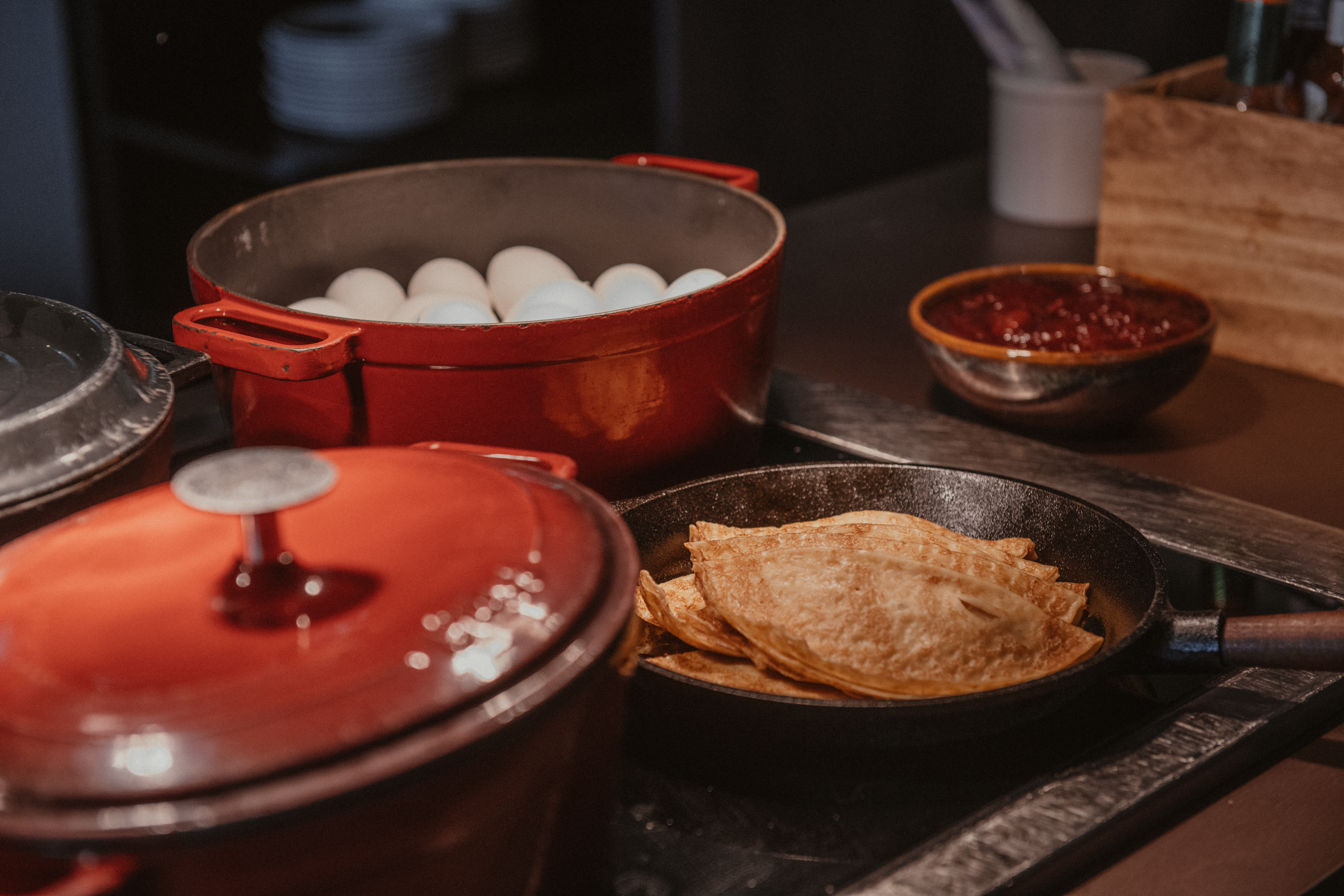 En buffé med en kastrull kokta ägg, en stekpanna med pannkakor och en skål med bärsylt, redo för frukost.