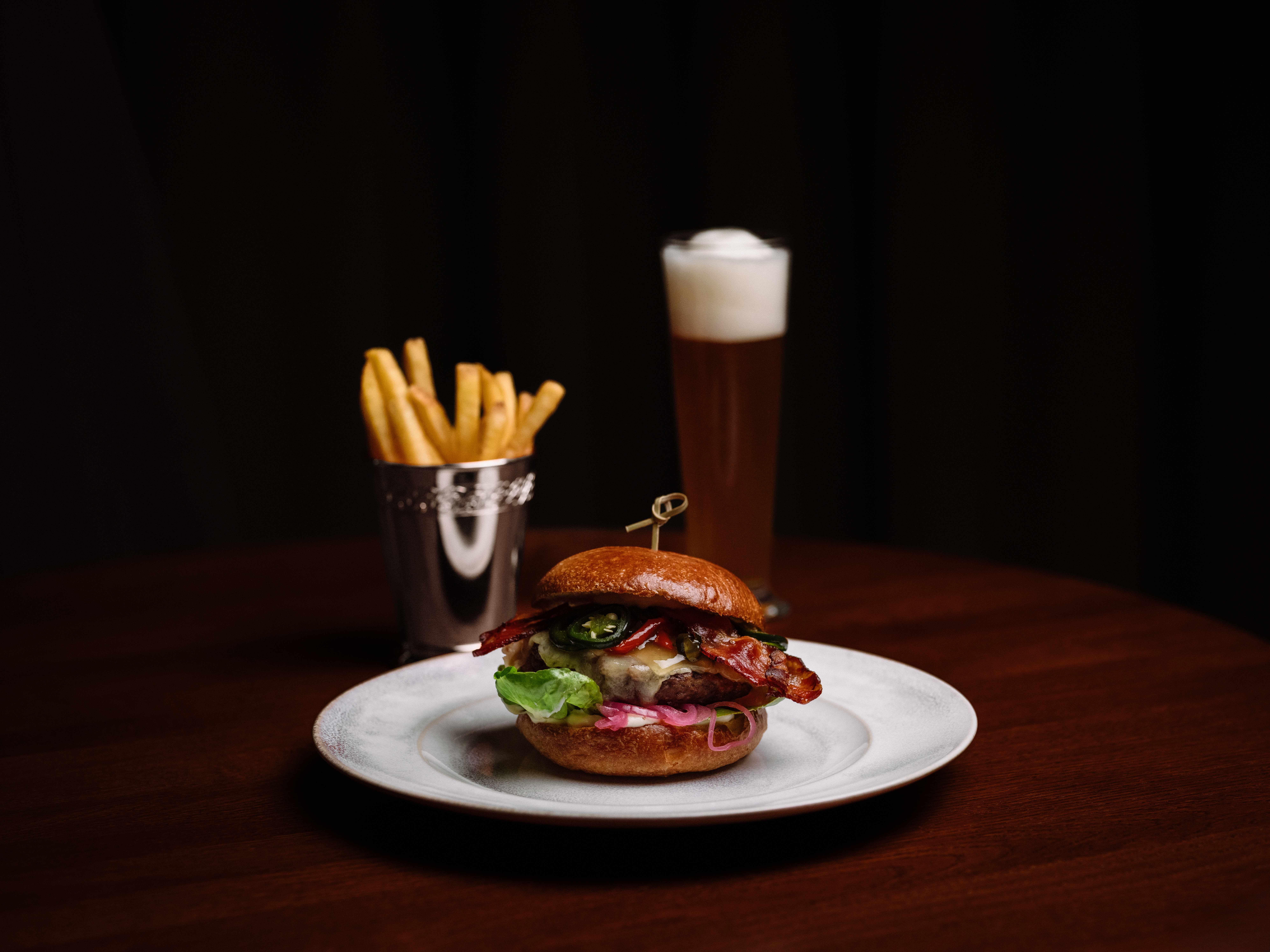 Herkullinen hampurilainen ranskalaisten ja oluen kera puupöydällä Hotel Kämp – Ravintola A La Kampissa.