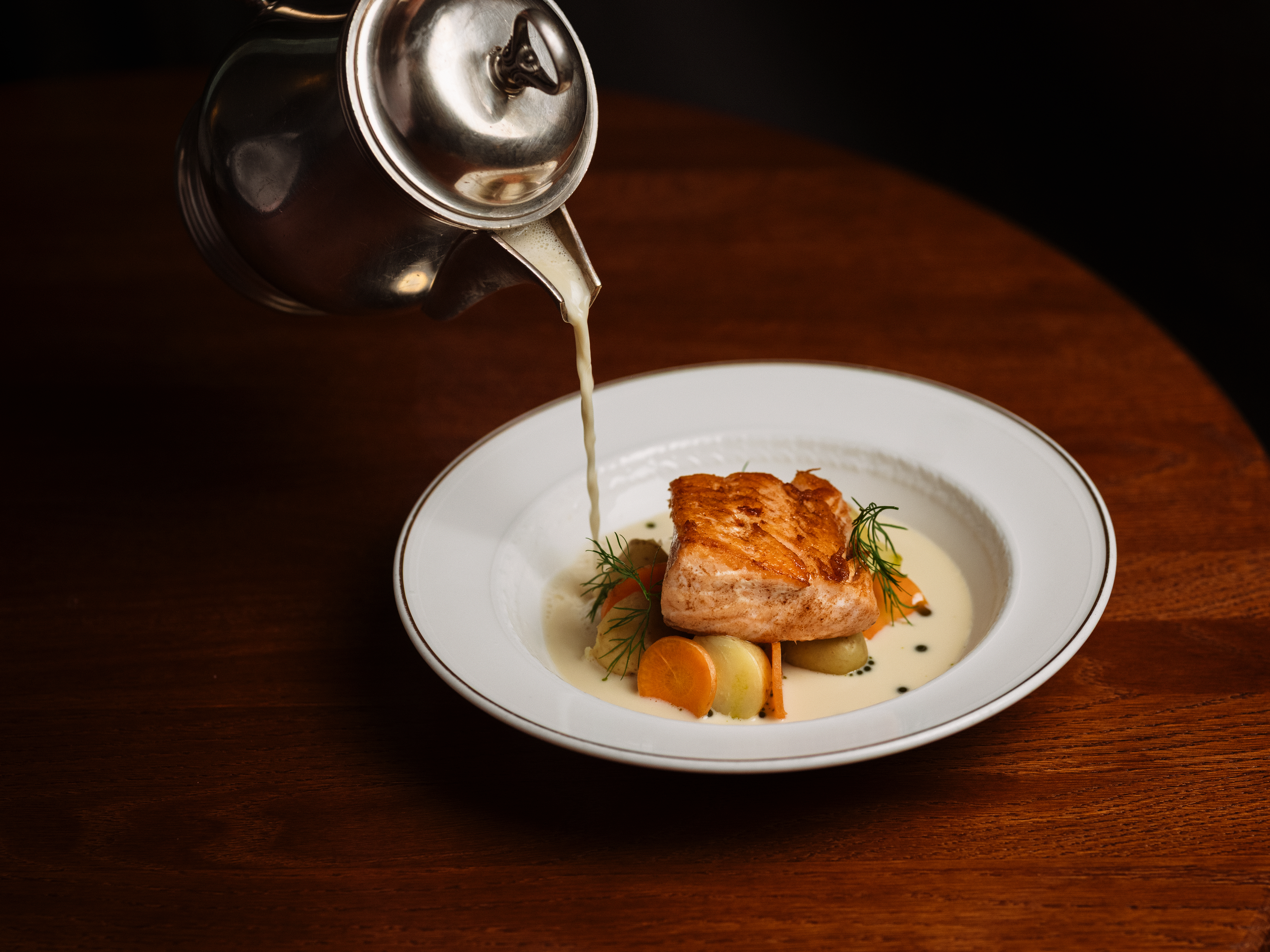 Tyylikäs lohi- ja kasvisruoka saa viimeisen silauksen, kun kermainen kastike kaadetaan hopeakannusta.