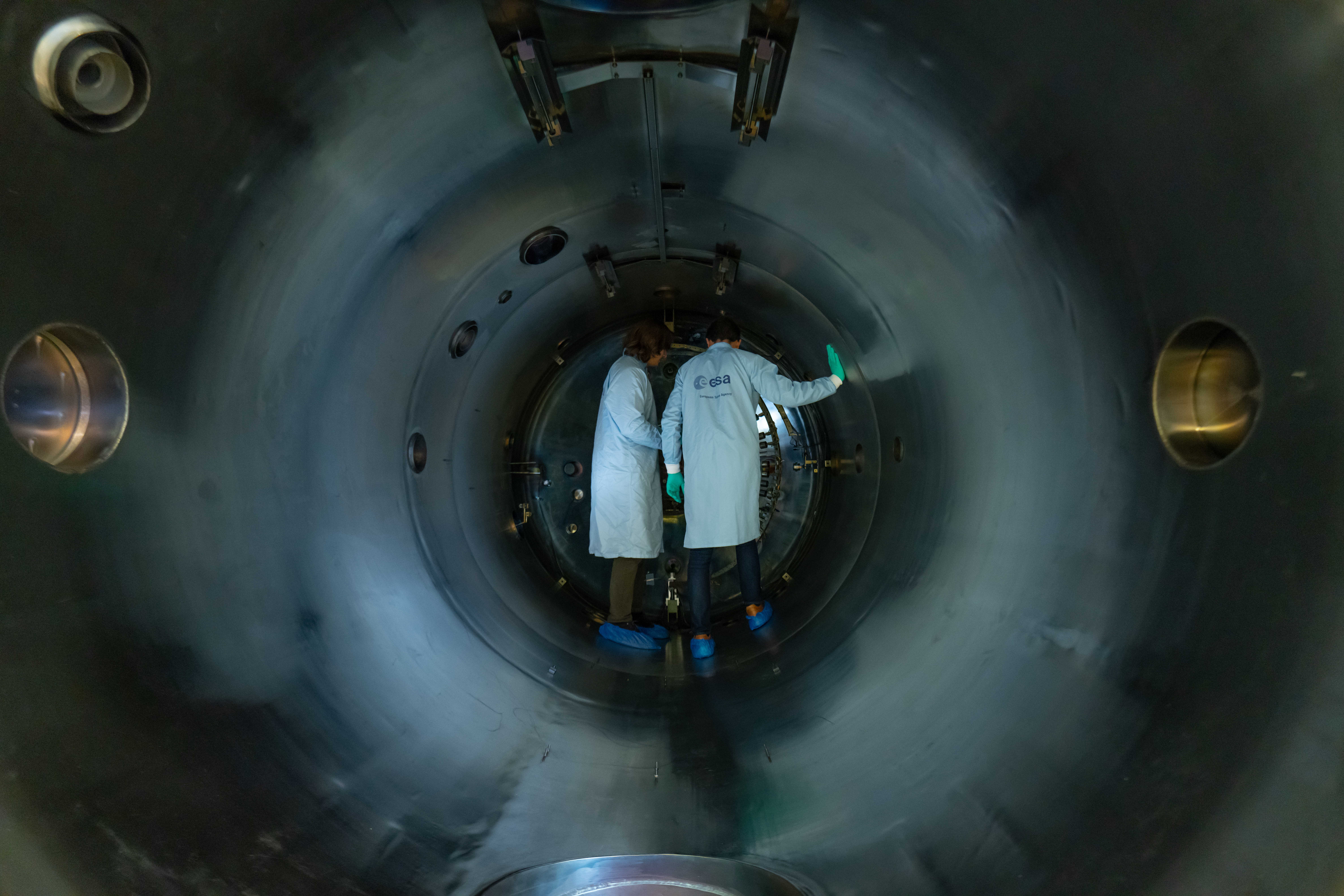 Engineers in ESA branded lab coats preparing a test inside a vacuum chamber