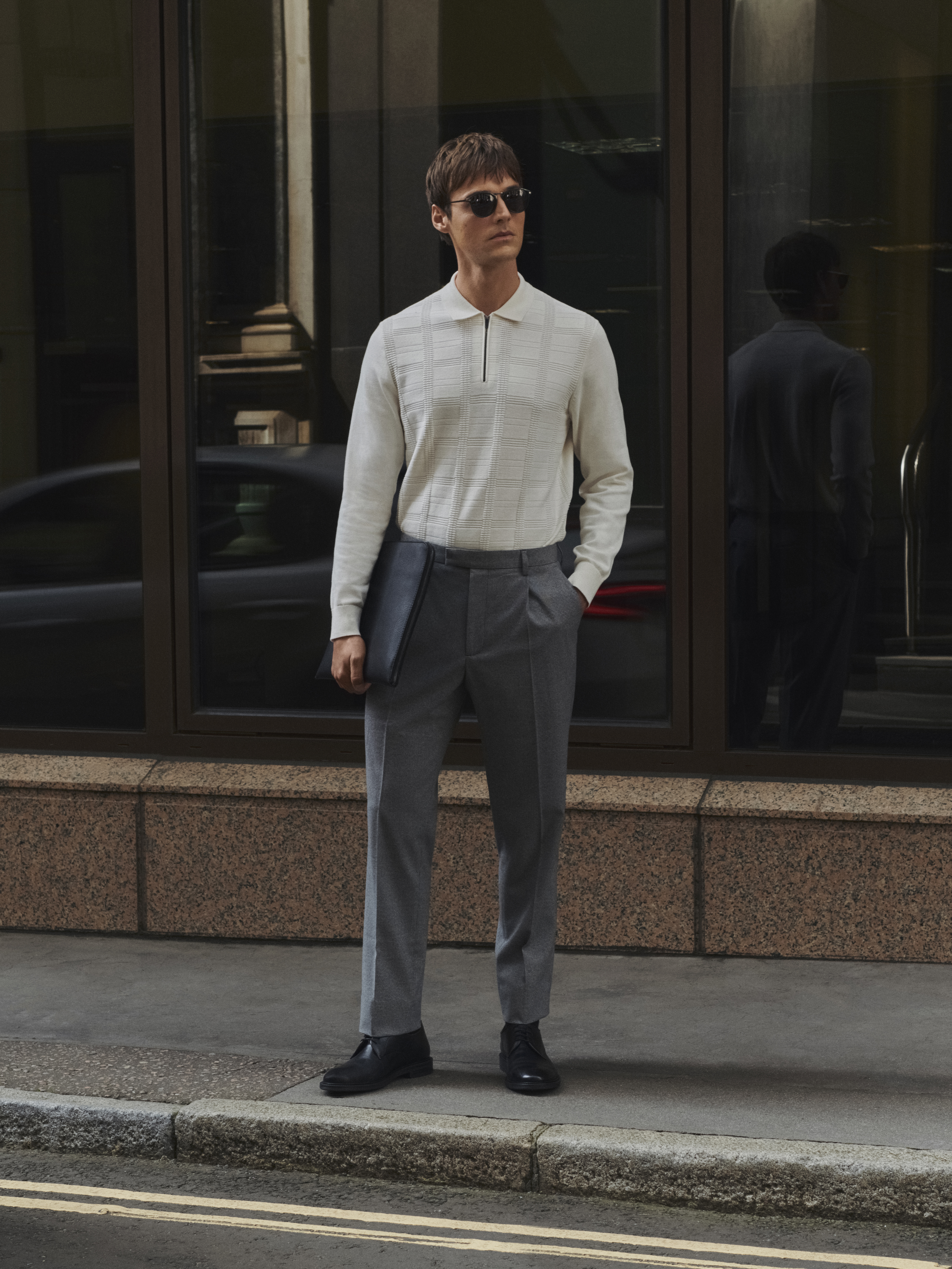 Man wearing ivory polo shirt, grey trousers and sunglasses