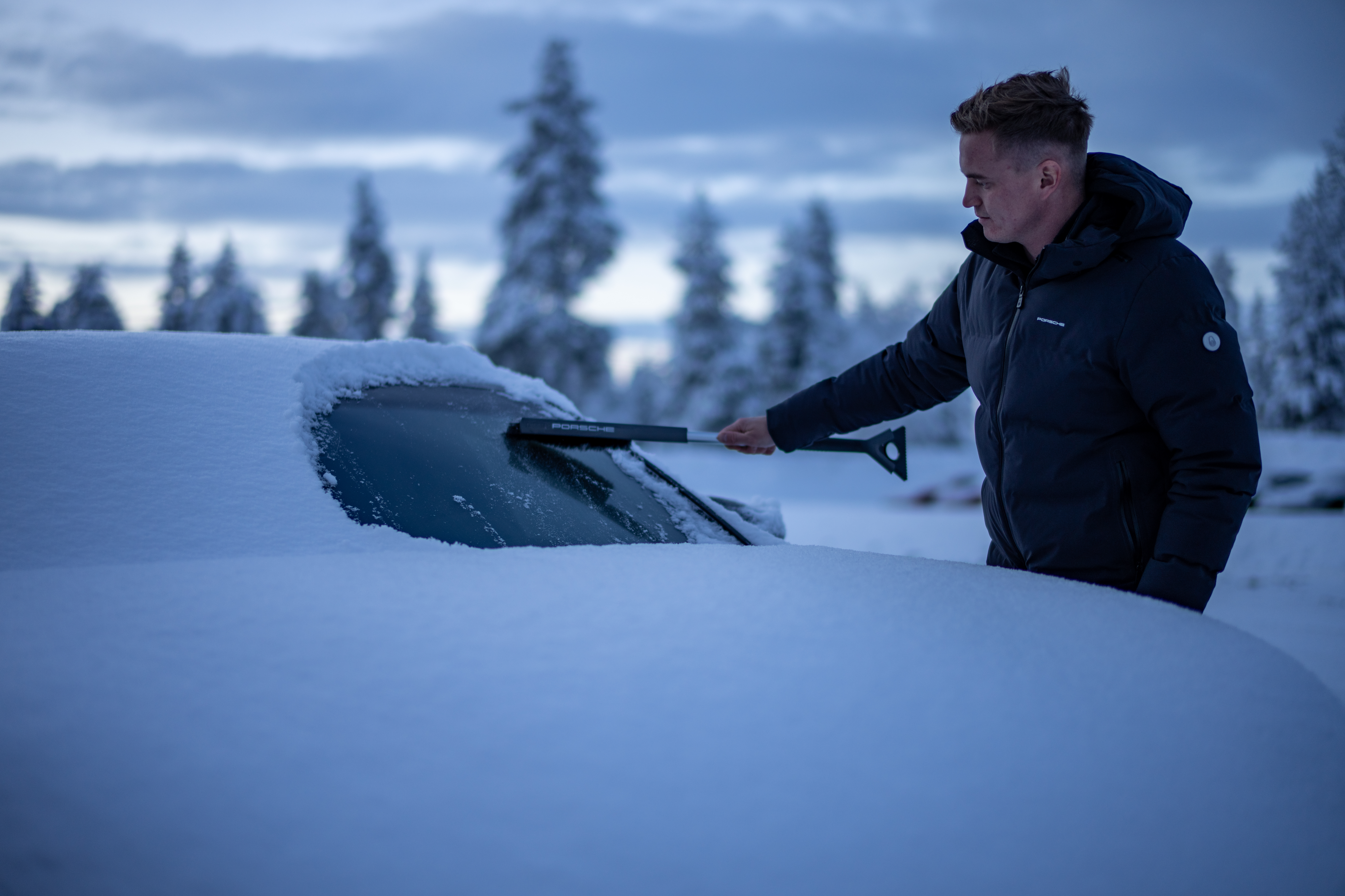 Man scrapes snow and ice from windscreen of Porsche Taycan