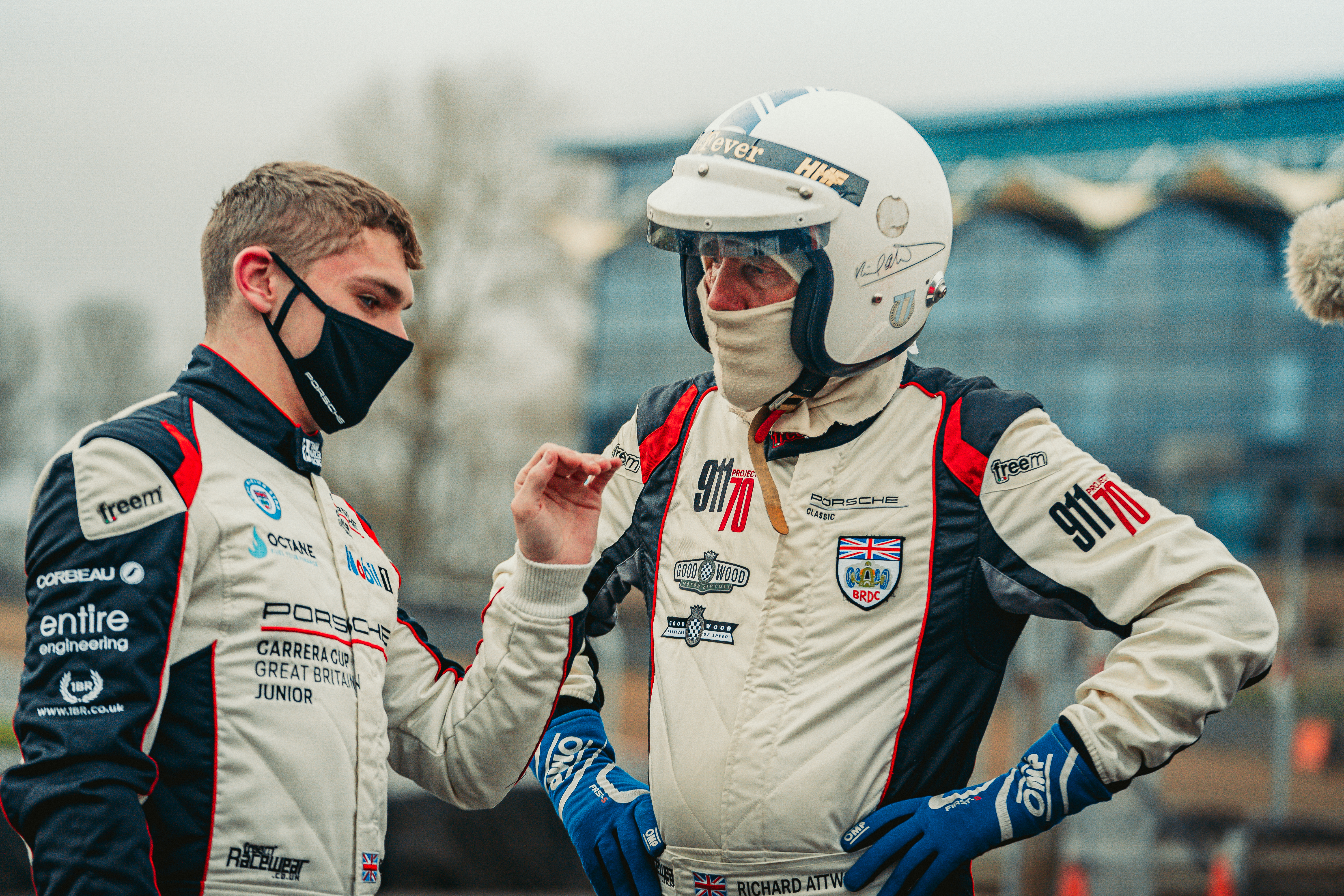Two drivers in racesuits, one in helmet, in discussion