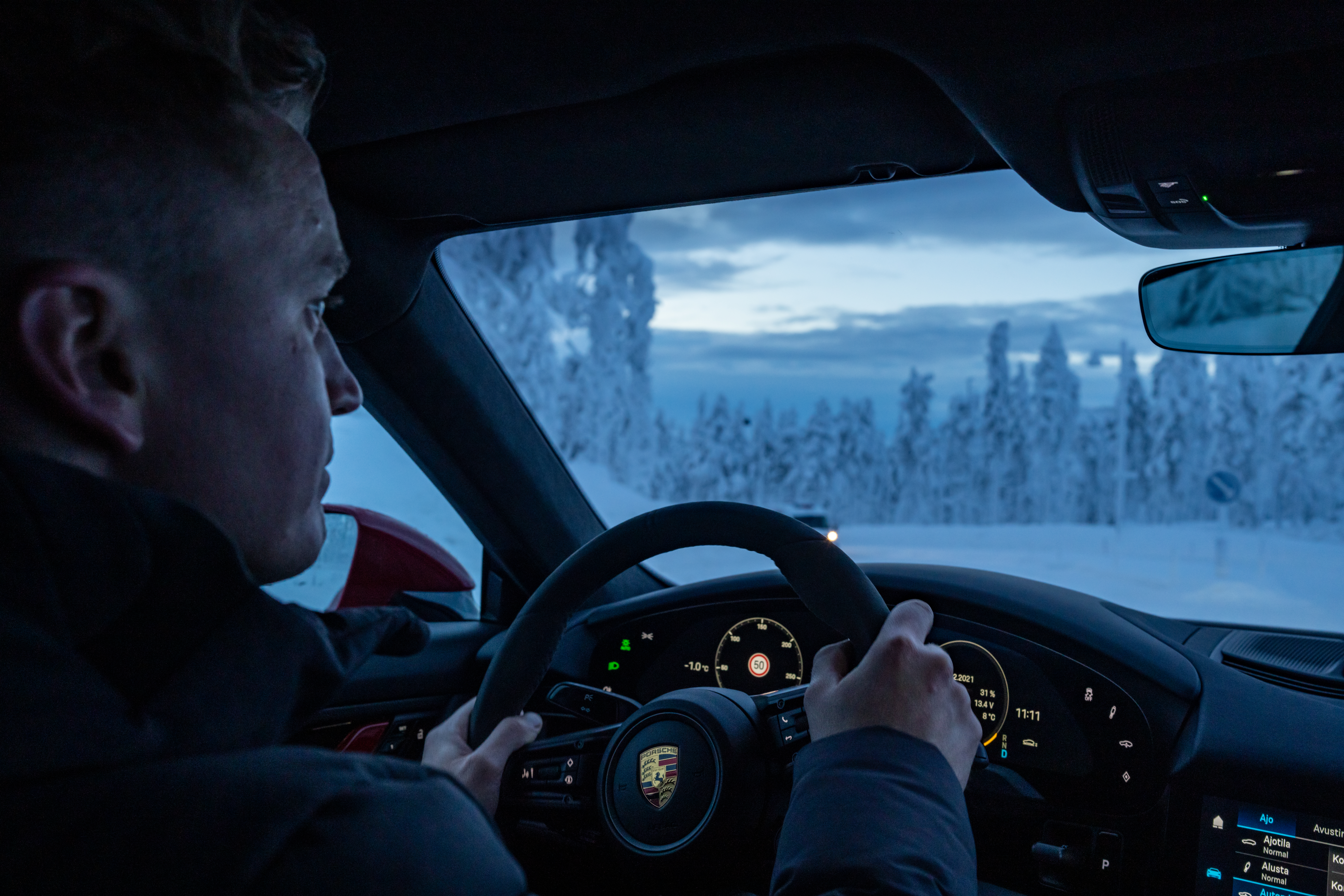 Inside a Porsche Taycan, man at wheel, on snowy road