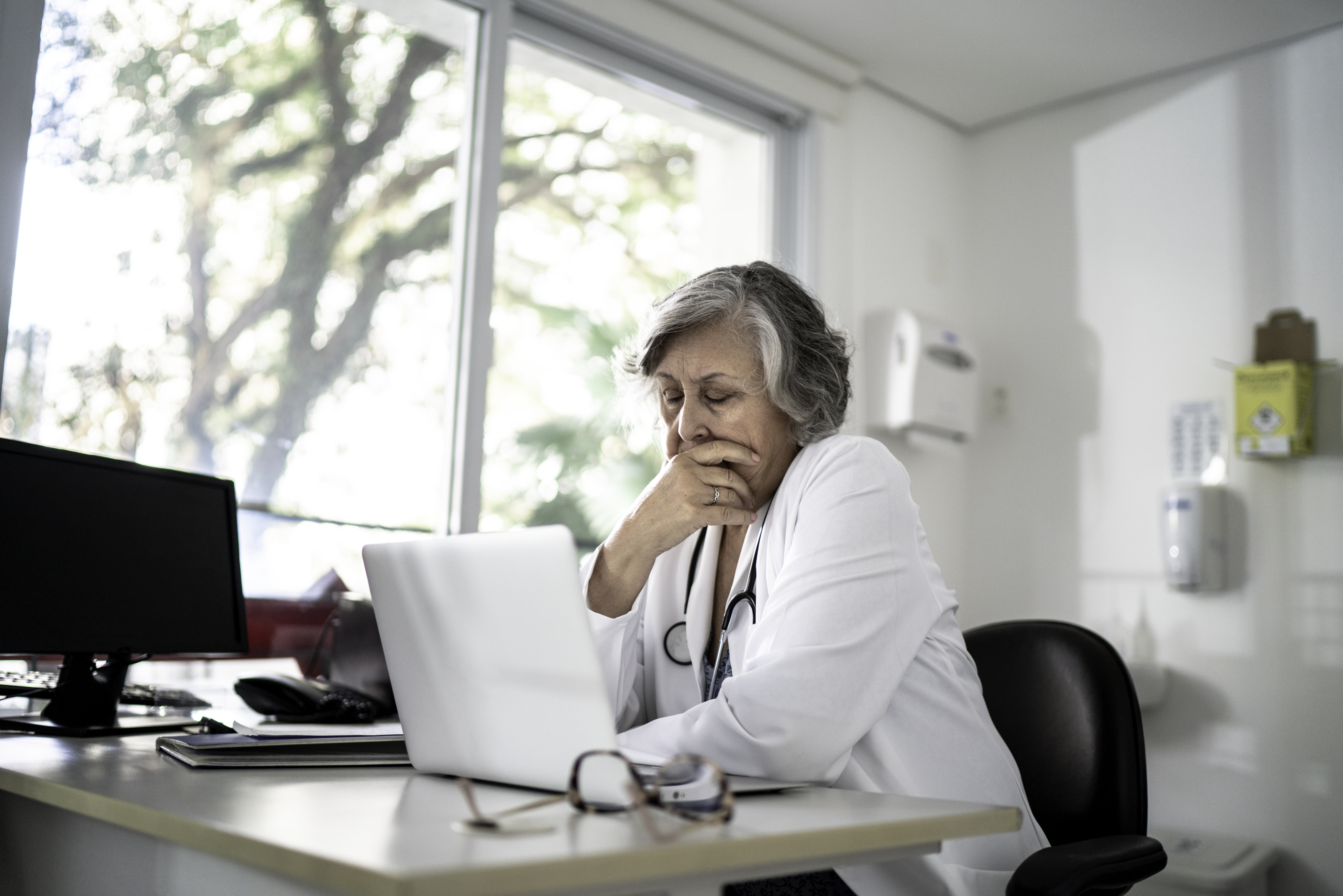 Overwhelmed healthcare worker looks at laptop.